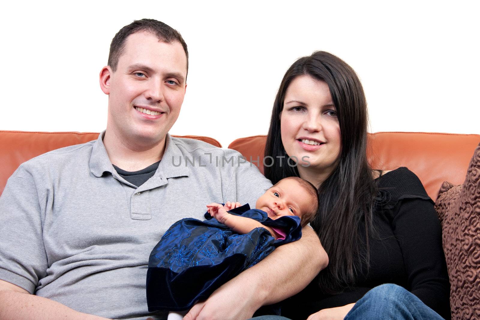 A young happy and healthy family seated on a couch holding their newborn daughter.