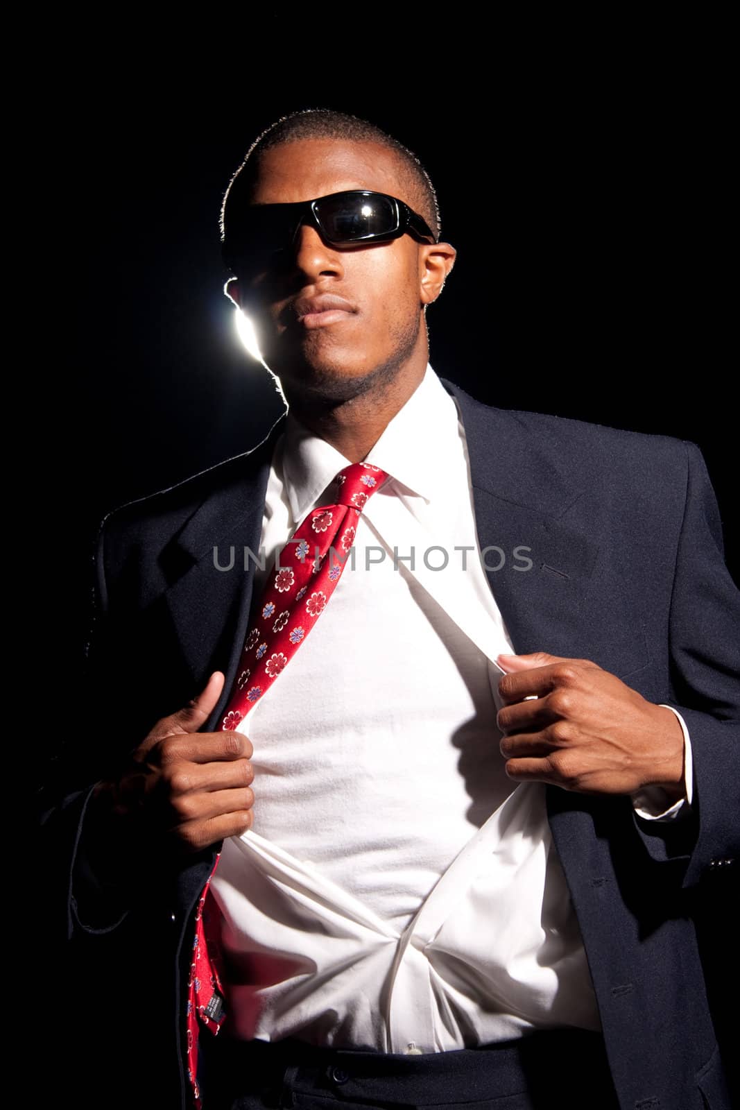 A young African American business man ripping his shirt open to reveal the t-shirt beneath. Add your text or artwork to easily customize the message.