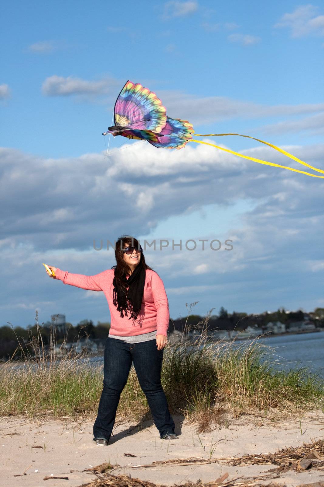 A young woman flies a kite at the beach on a nice day.