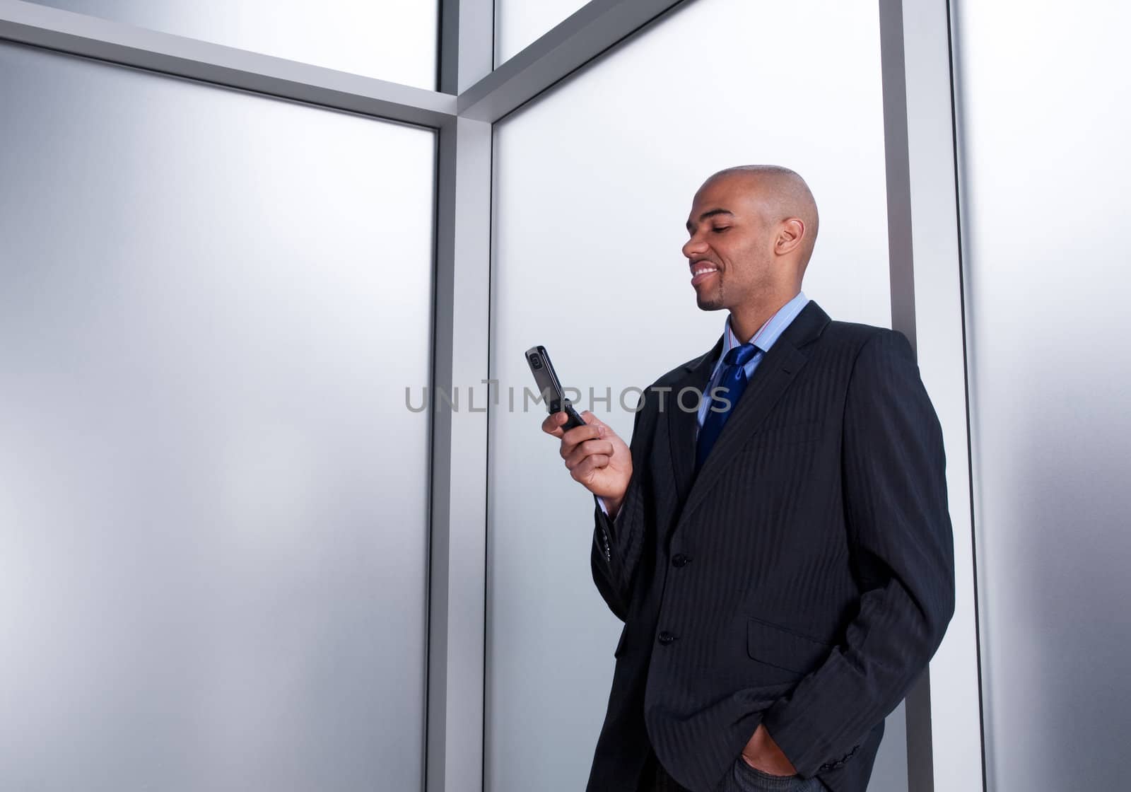 Young businessman beside an office window looking at his cell phone, smiling.
