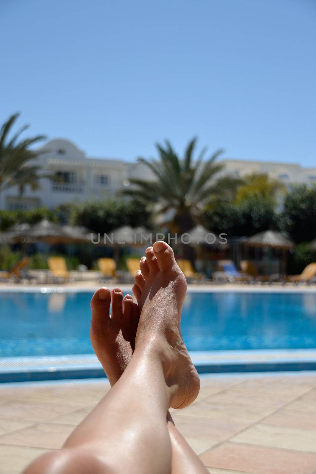 Legs of young woman relaxing at tropical pool.