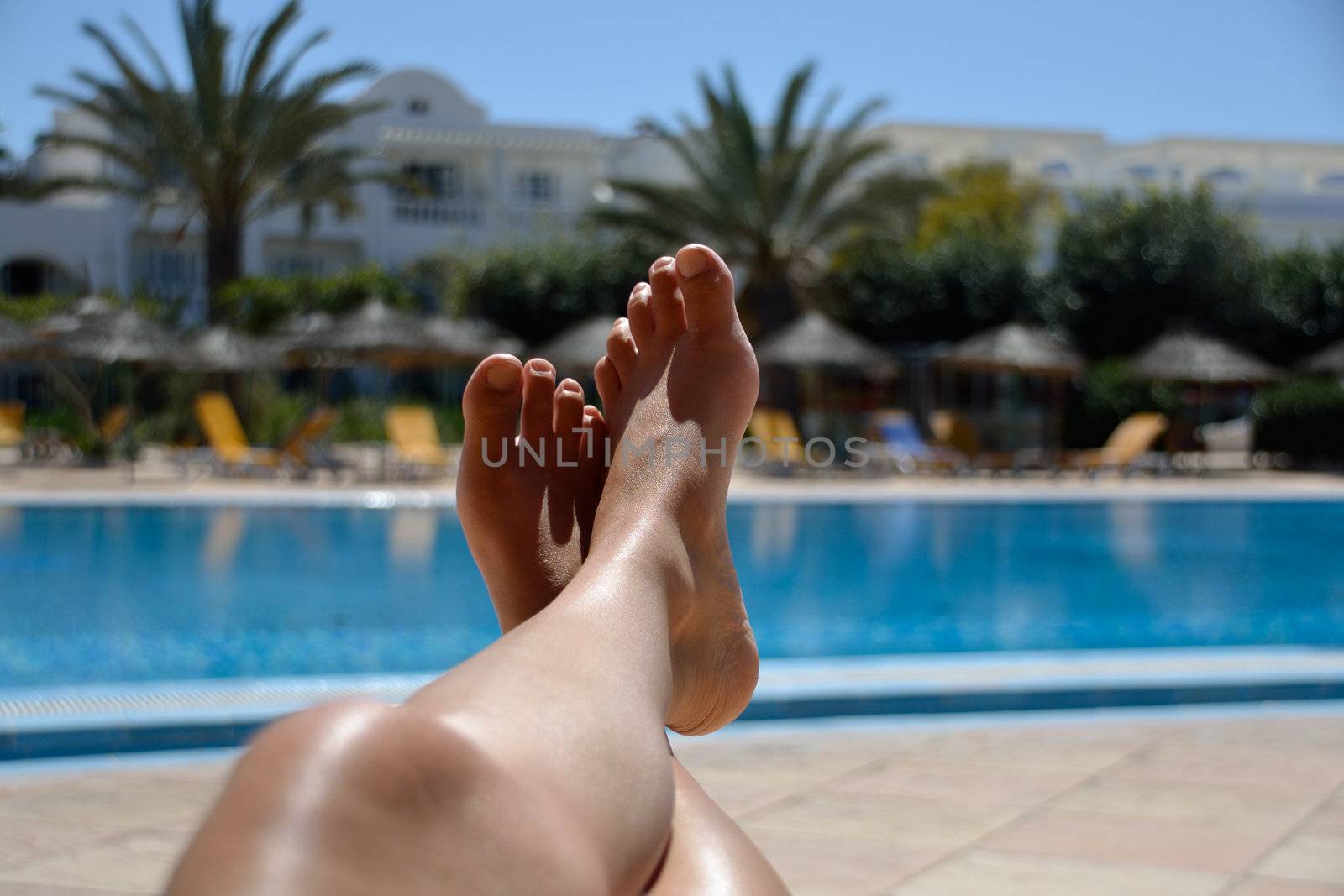 Legs of young woman relaxing at tropical pool.