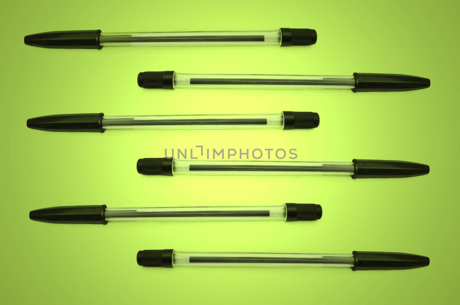Six black biro pens arranged horizontally in formation over green and yellow light effect