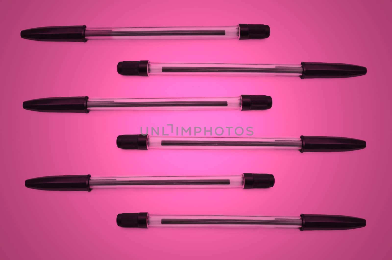 Six black biro pens arranged horizontally in formation over pink light effect