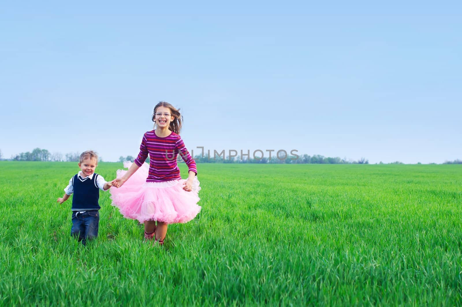 A beautiful sister runing with her cute little brather on the grass