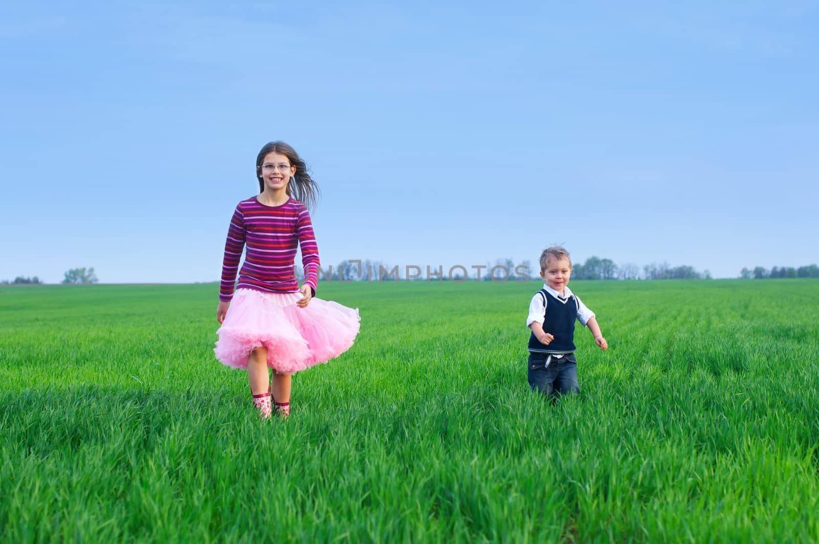 A beautiful sister runing with her cute little brather on the grass
