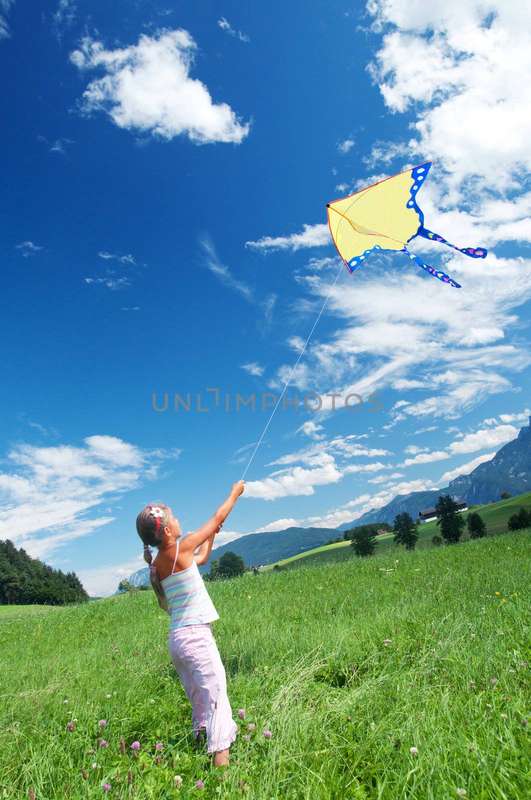 Cute child flying a kite in the bright blue sky. Vertical view