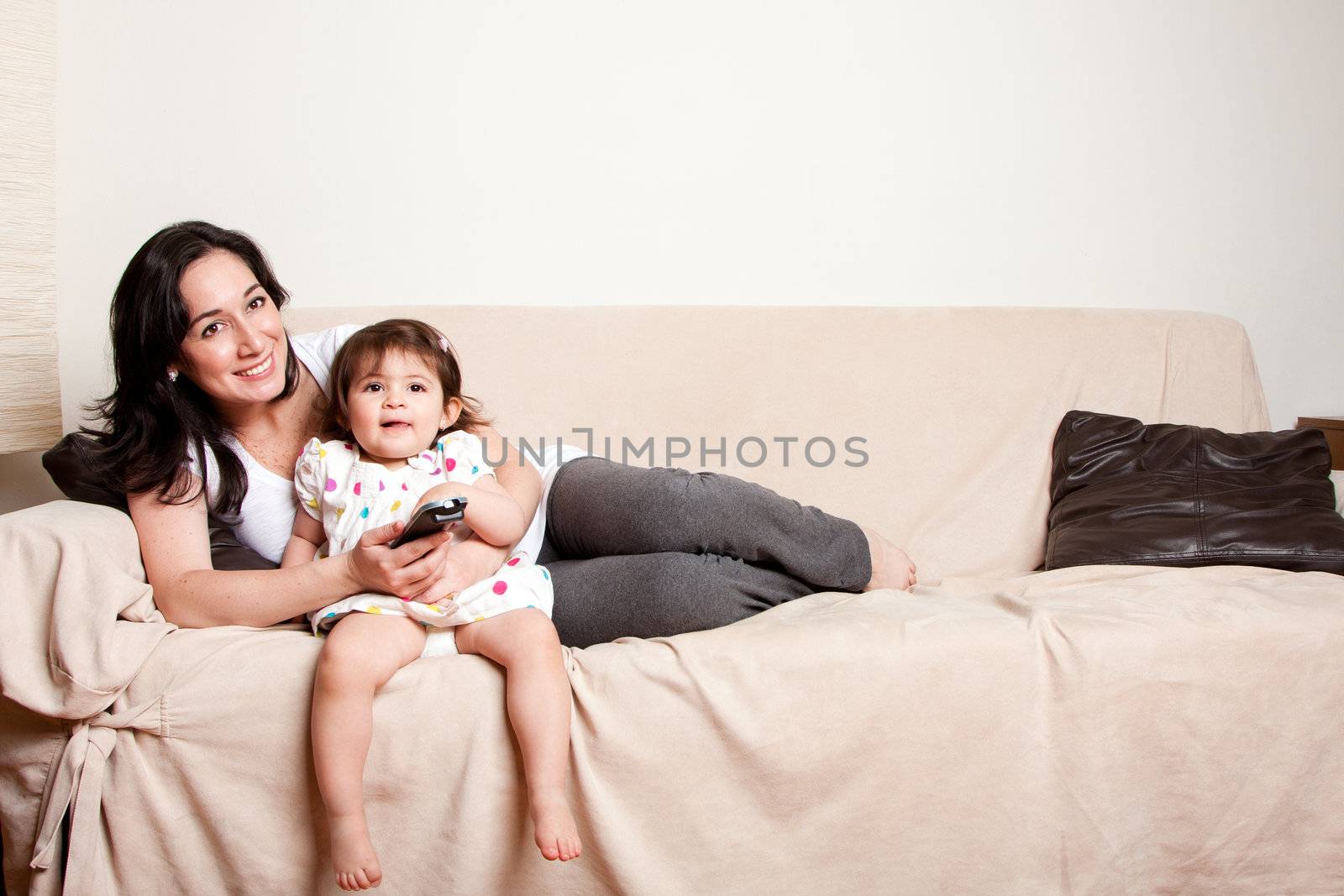 Beautiful happy family mother and baby toddler daughter sitting relaxed laid back on sofa couch in livingroom watching TV television.