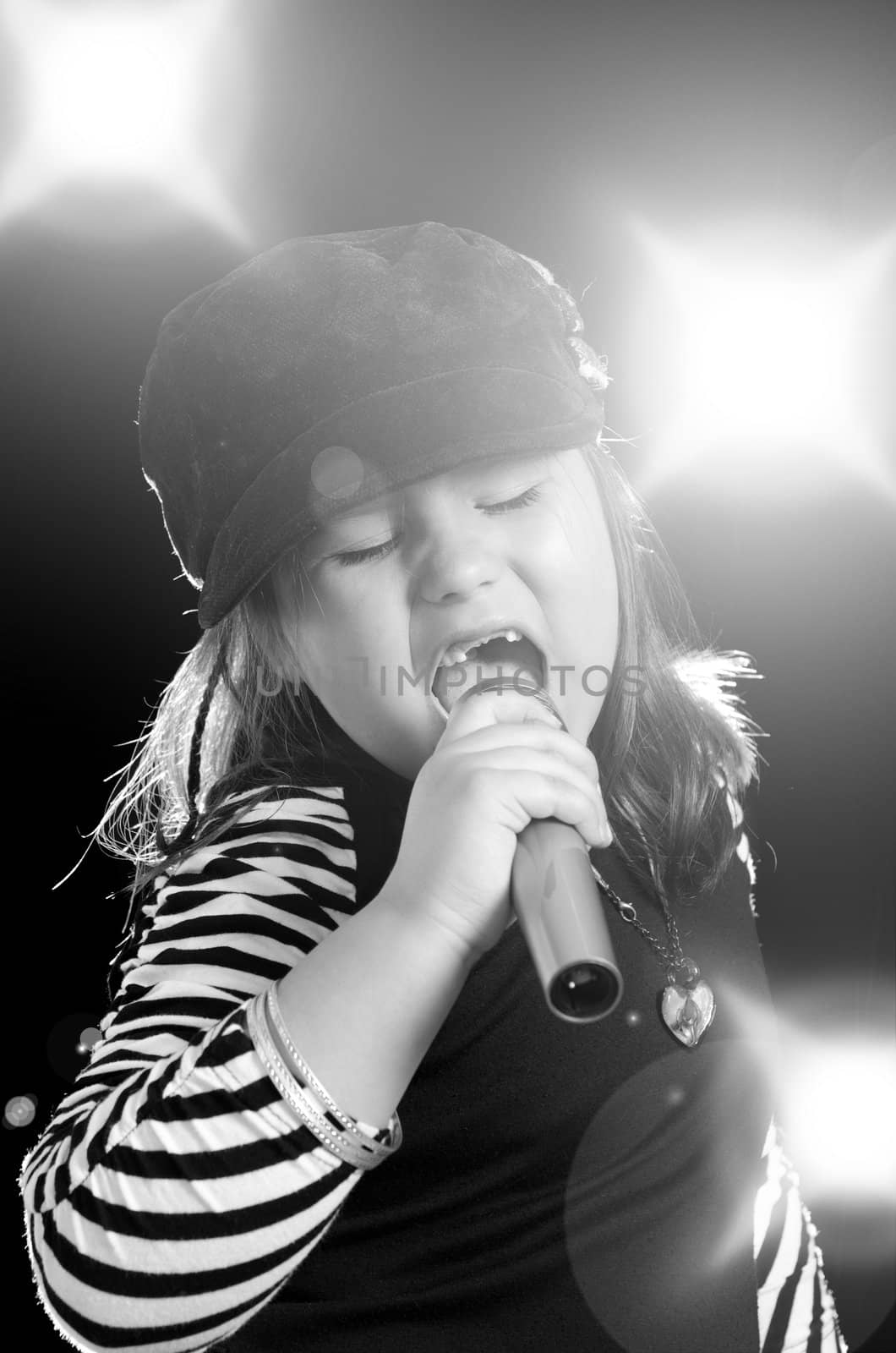 A little girl is singing into a microphone with flashes and lights in the background.