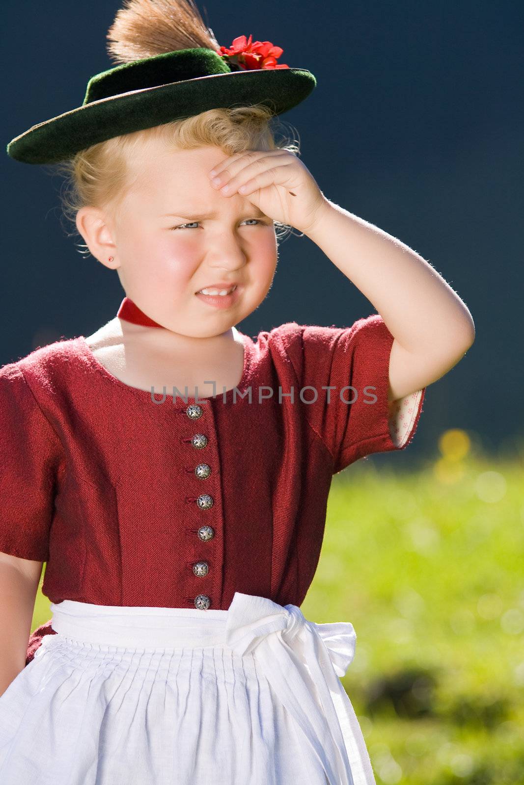 Little blonde girl in typical Bavarian costume on the mountain and looks into the country