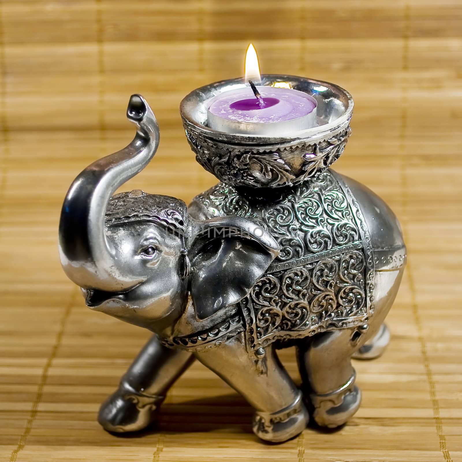 silver elephant statue with little purple candle over wooden texture