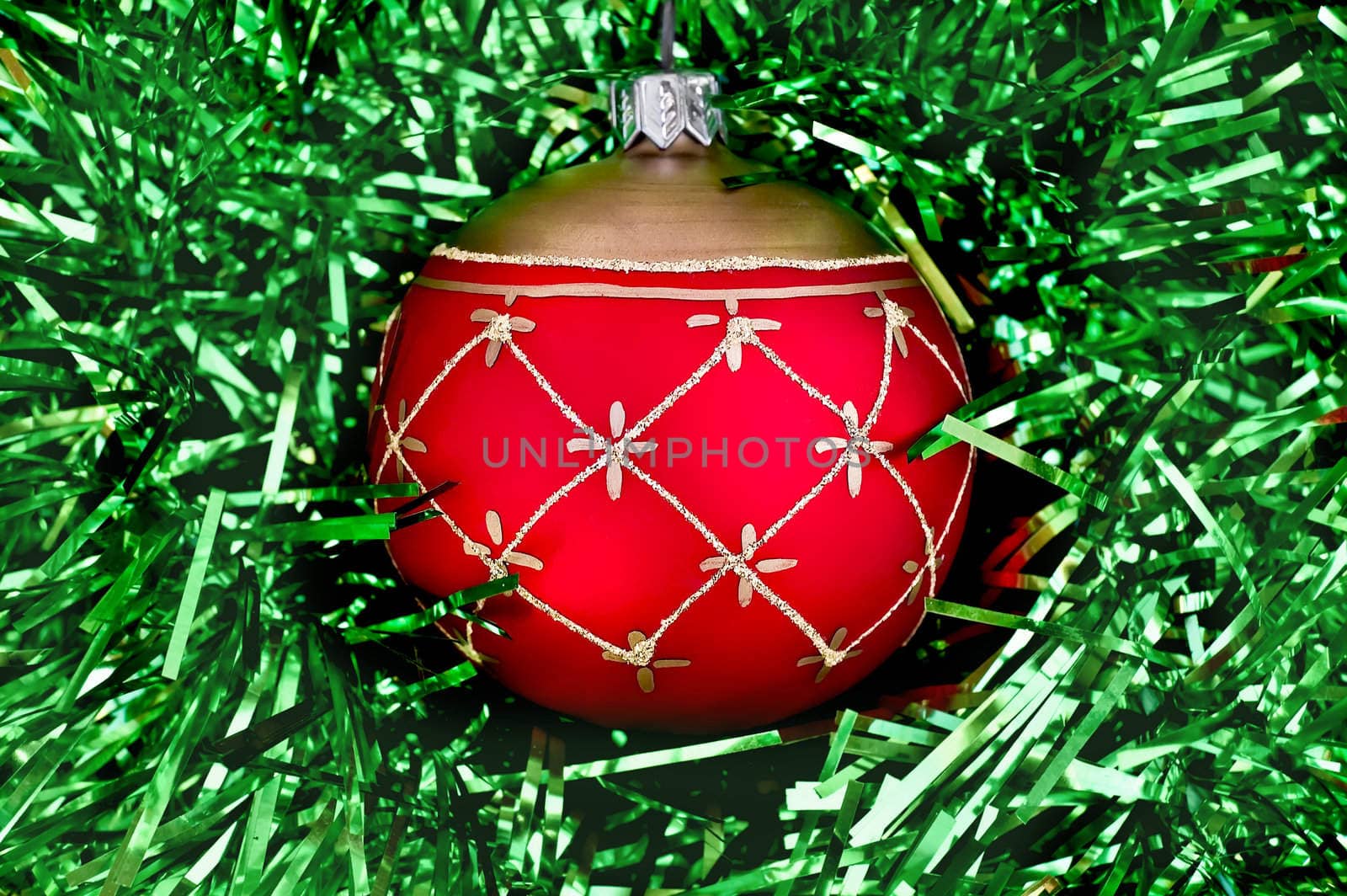 Christmas red ball with golden patterns on a background of green tinsel