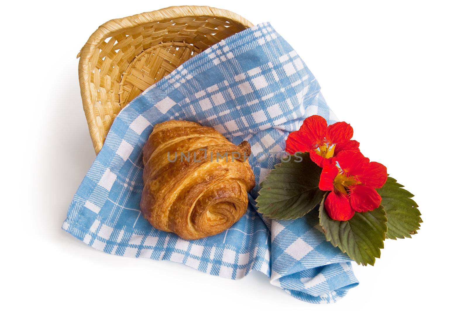 Golden croissant on a checkered blue cloth, in a wicker basket with red flowers isolated on white background