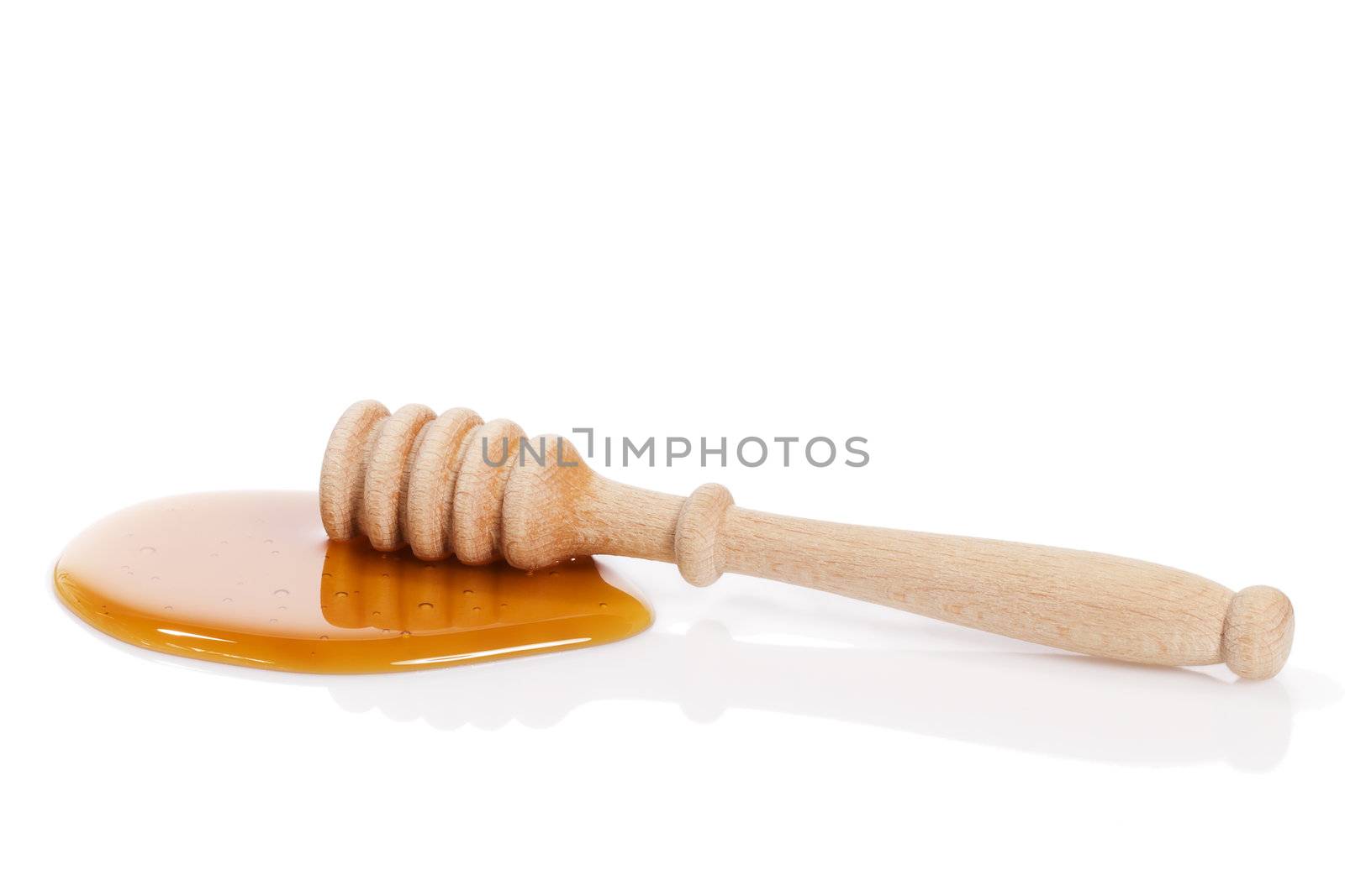 dry honey dipper in a puddle of honey on white background