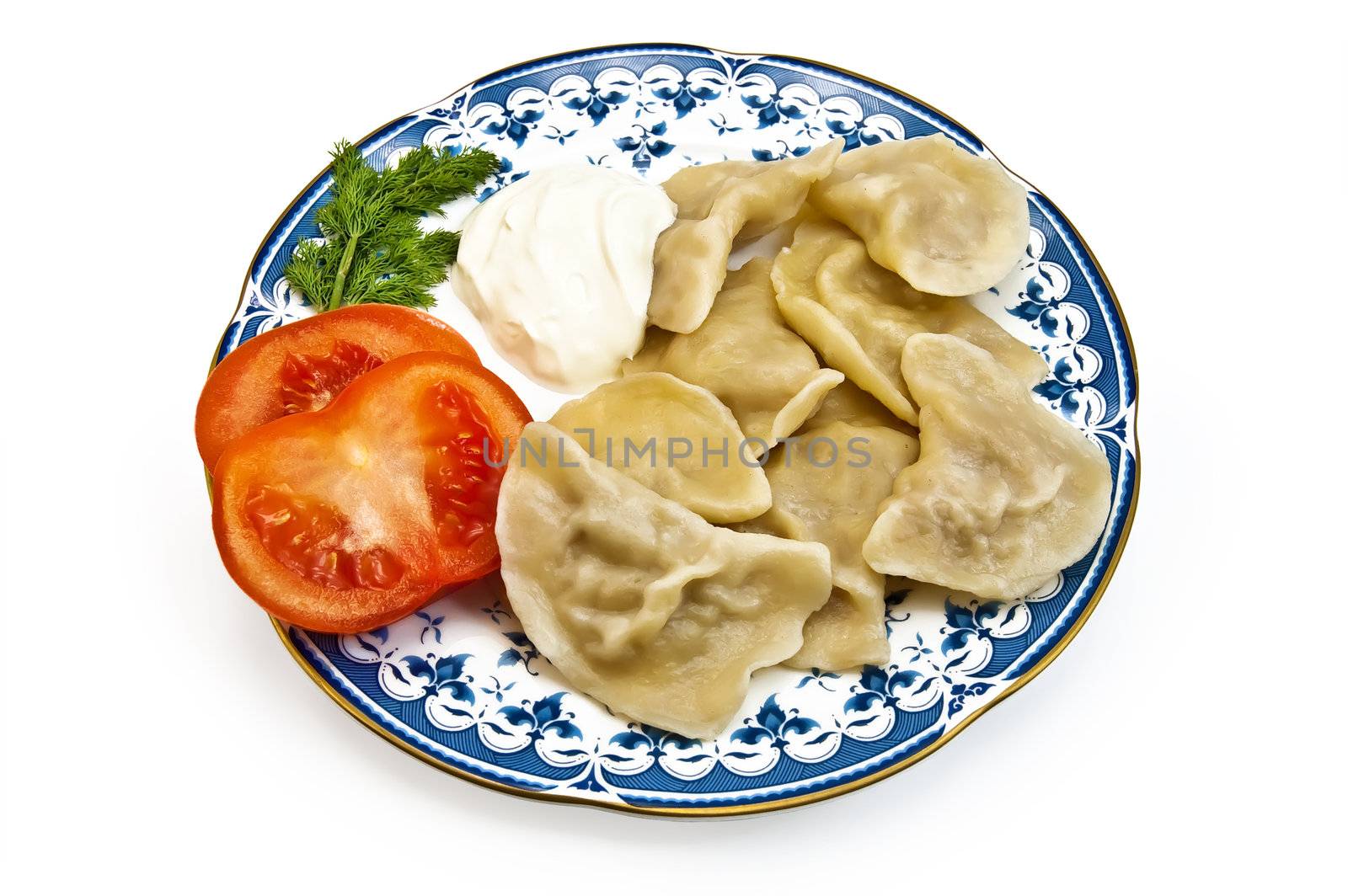 Dumplings, two slices of tomato, a sprig of dill and sour cream on the porcelain plate isolated on white background