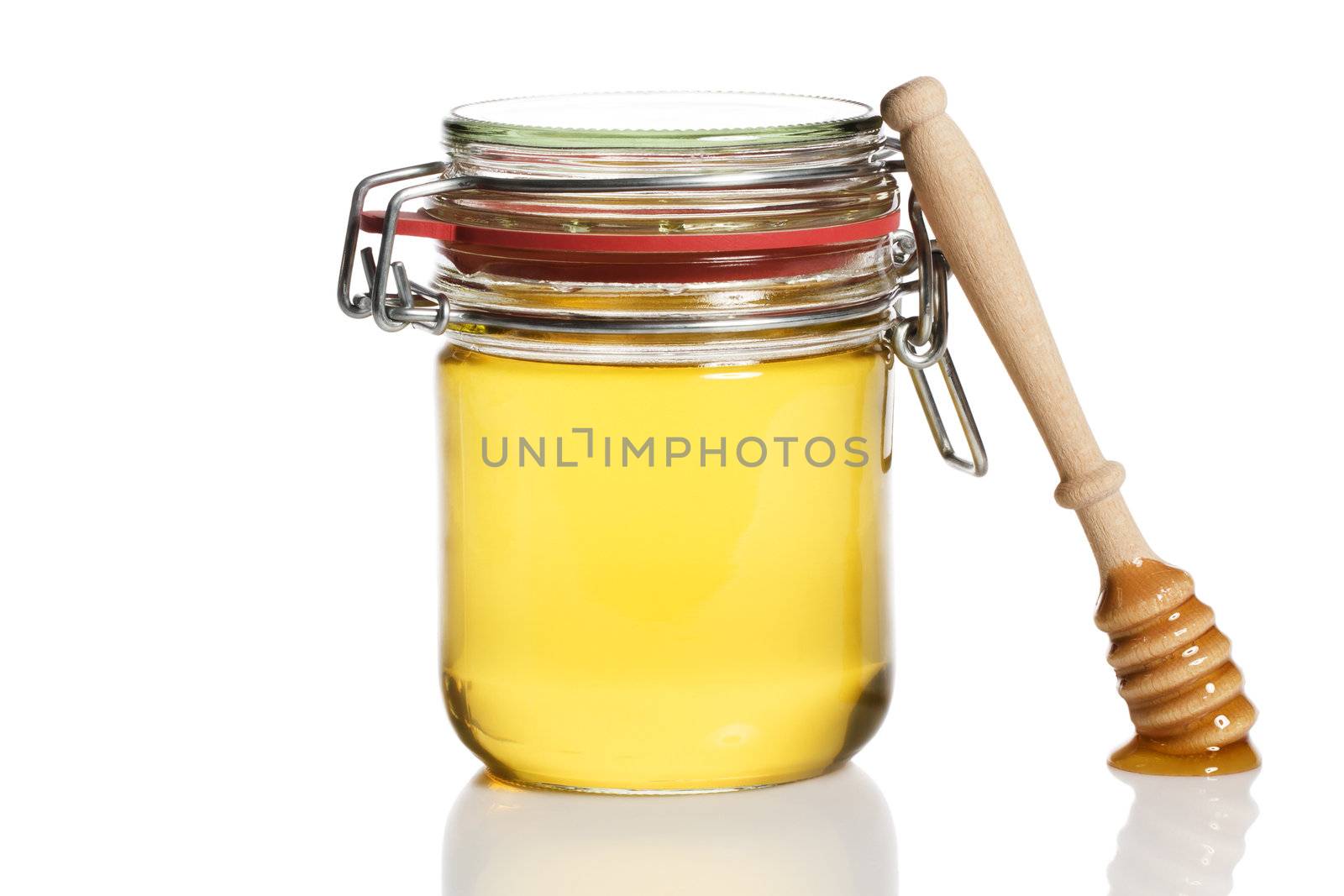 honey covered honey dipper leaning at a honey jar on white background