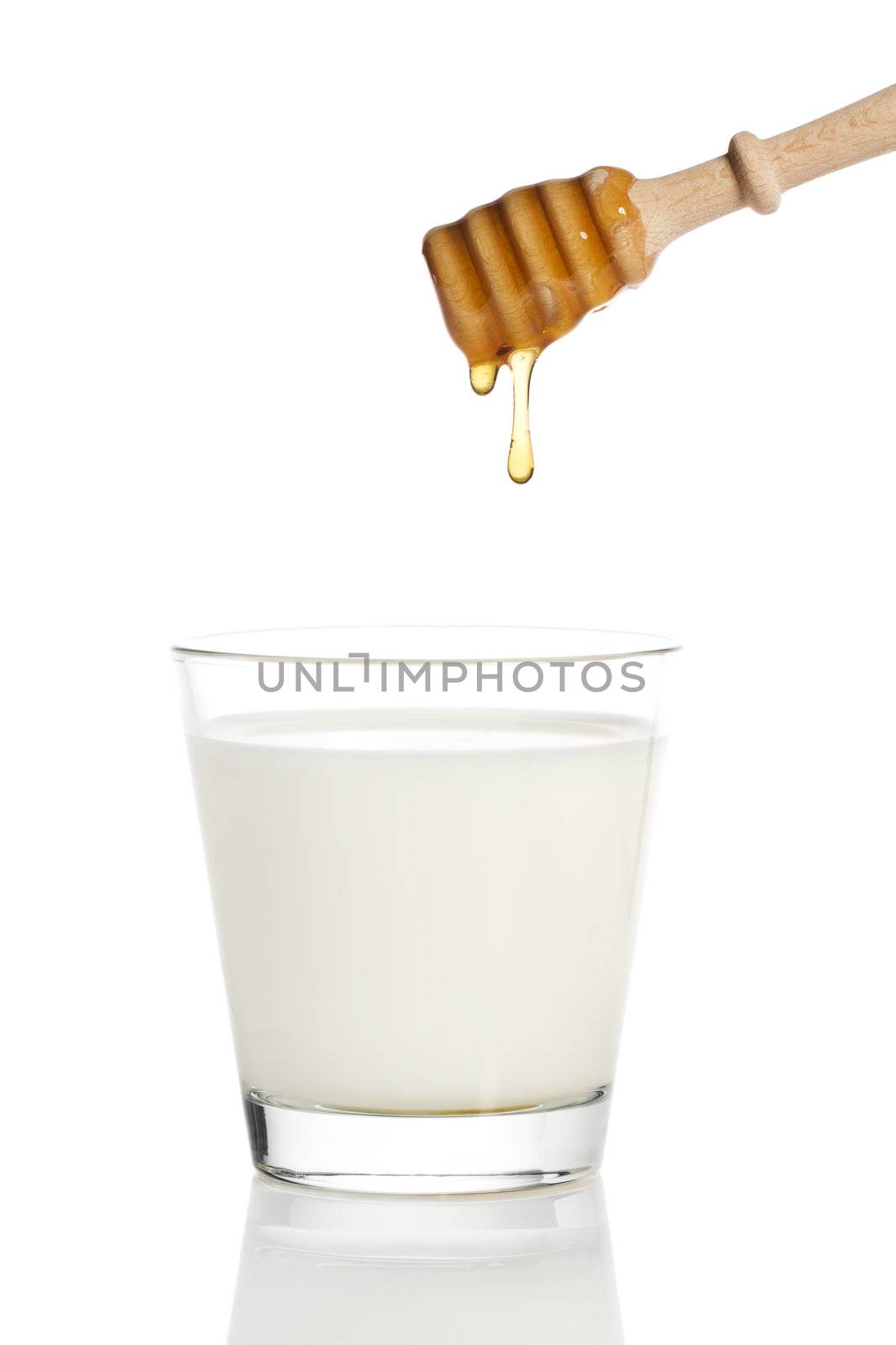 honey drops from a honey dipper in a glass of milk on white background