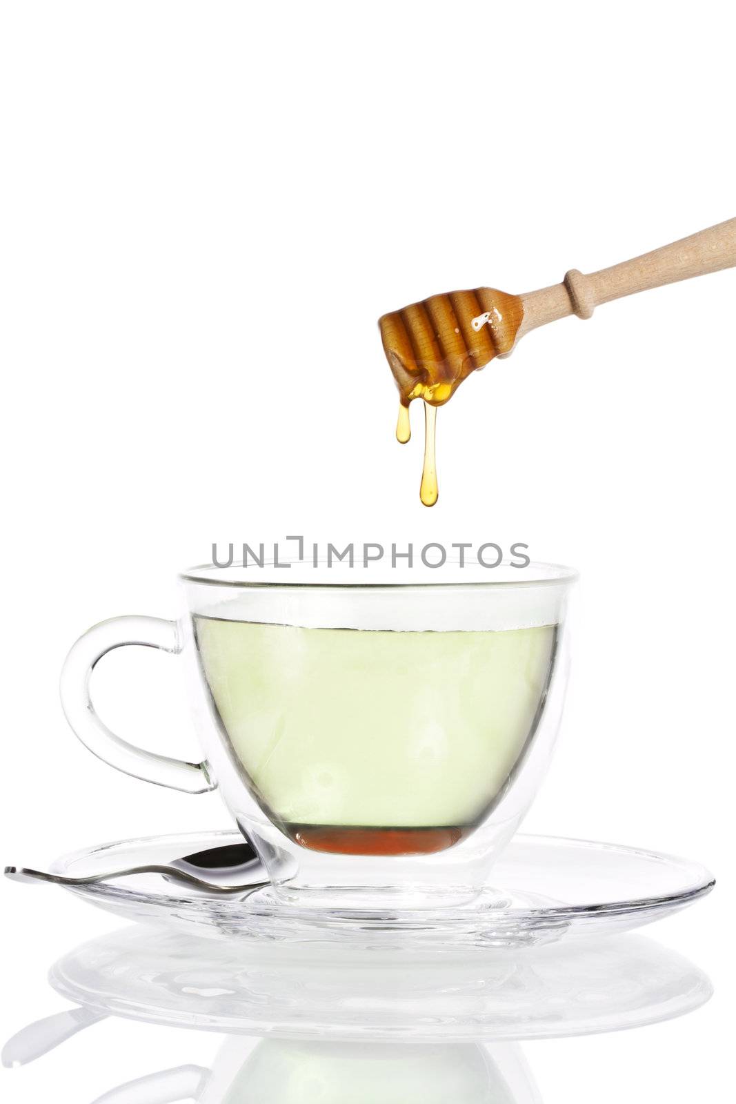 honey drops from a honey dipper in glass cup with green tea on white background