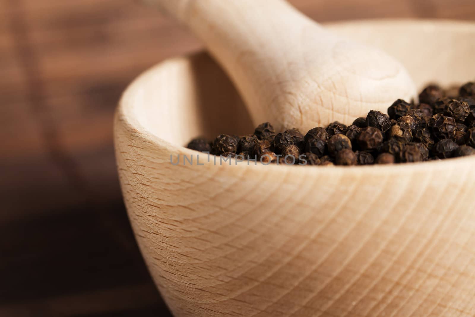 closeup of peppercorns in a wooden mortar with a very soft focus