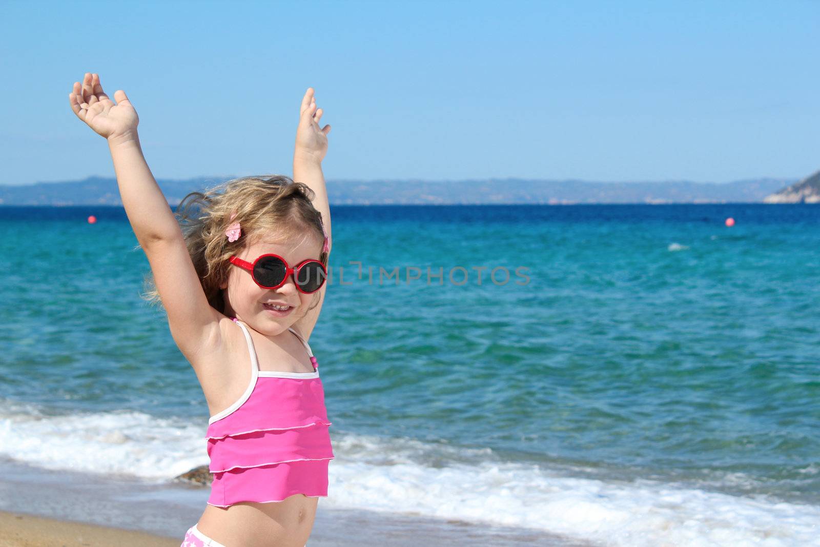 happy little girl with sunglasses and hands up on the beach