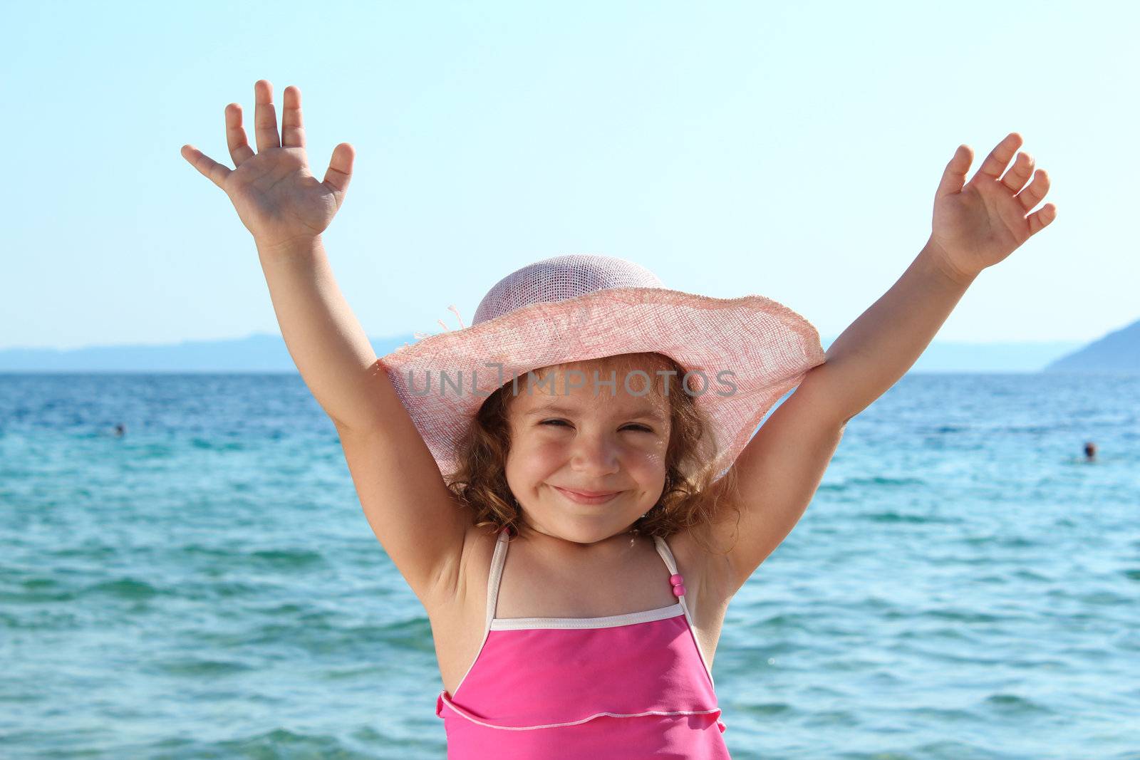 happy little girl with straw hat and hands up on the beach by goce