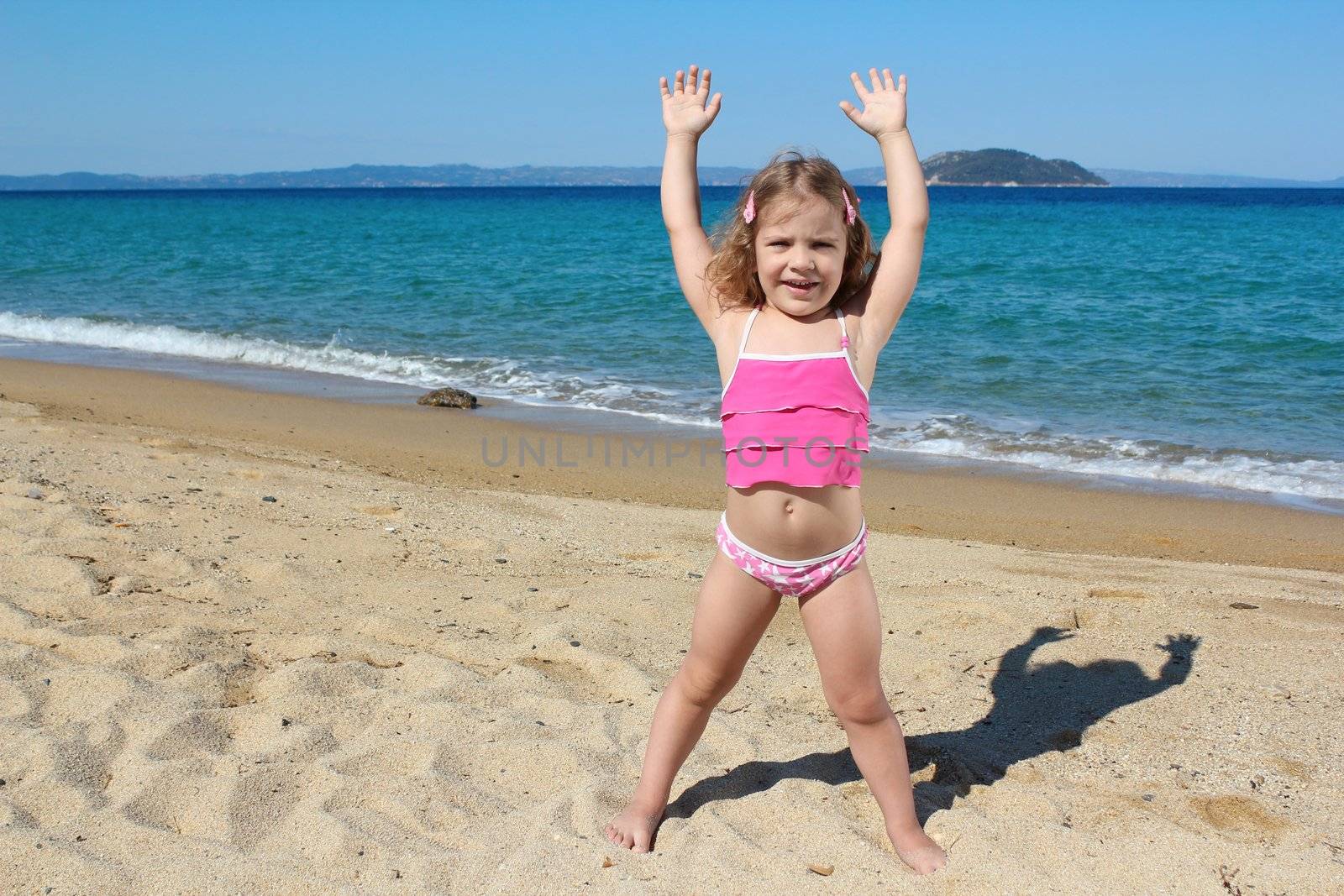 little girl with hands up standing on the beach by goce
