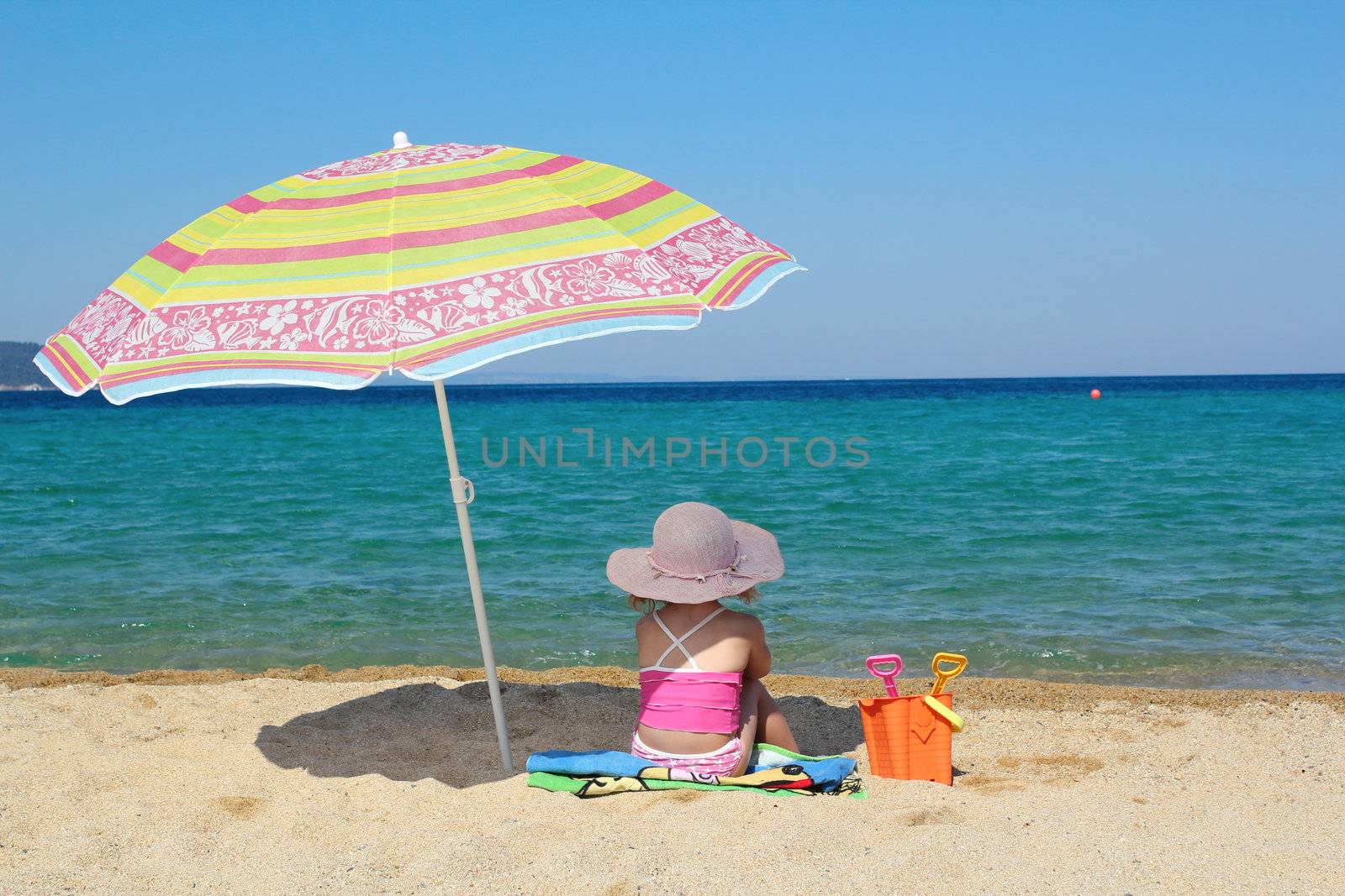 little girl sitting on beach under sunshade by goce