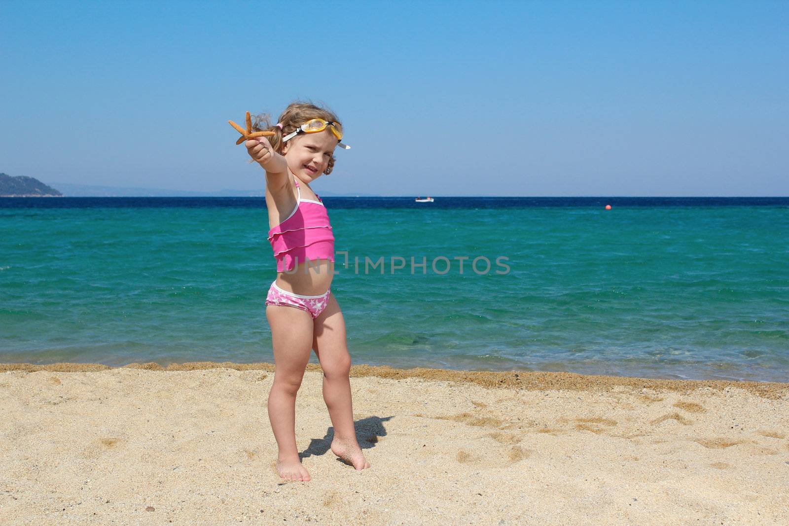 little girl with starfish and goggles on beach by goce