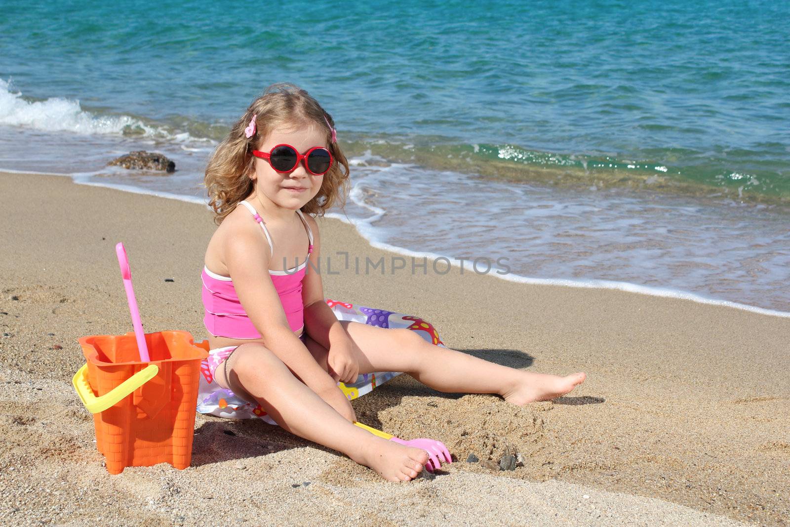 little girl with sunglasses playing on beach by goce
