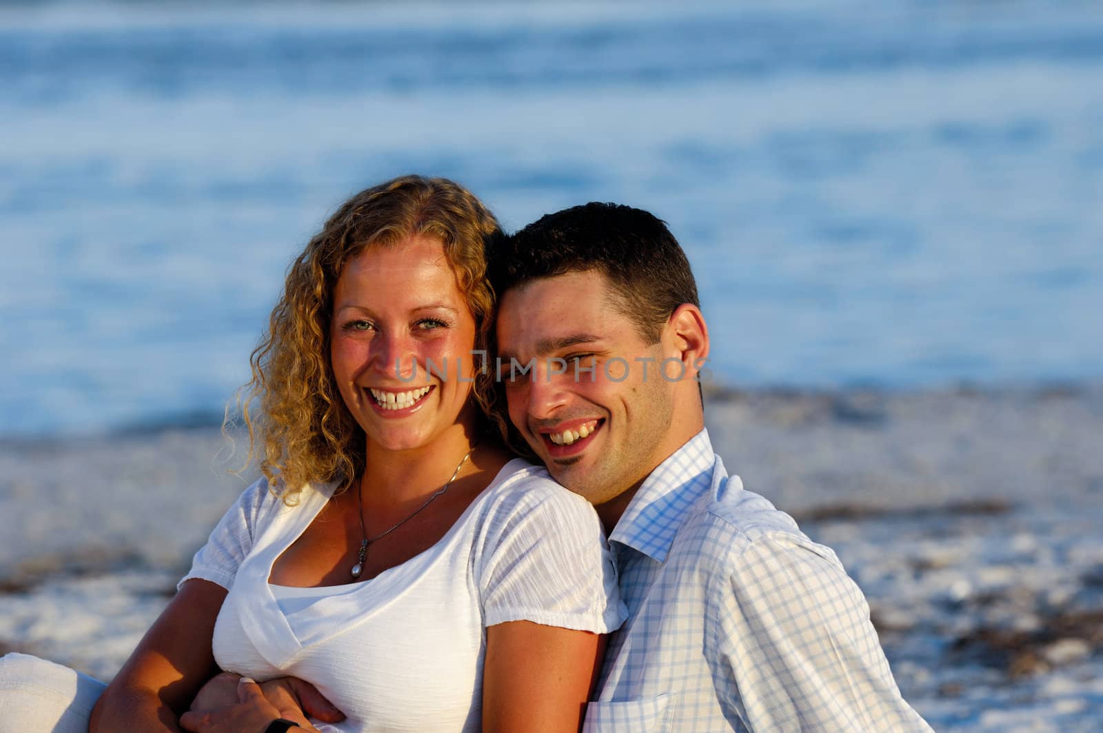A sweet young couple is sitting together on beach.