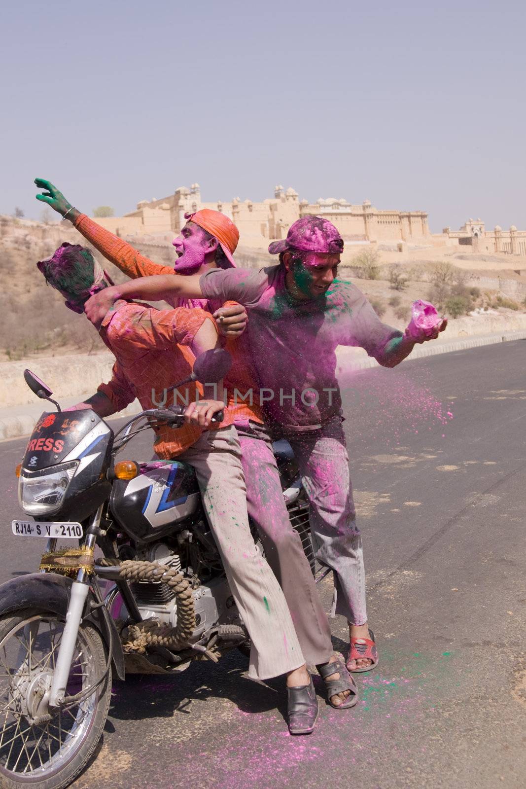 Group of young Indians on a motorbike covered in colored paint from celebrating the Hindu Festival of Holi outside Amber Fort in Jaipur, Rajasthan, India.