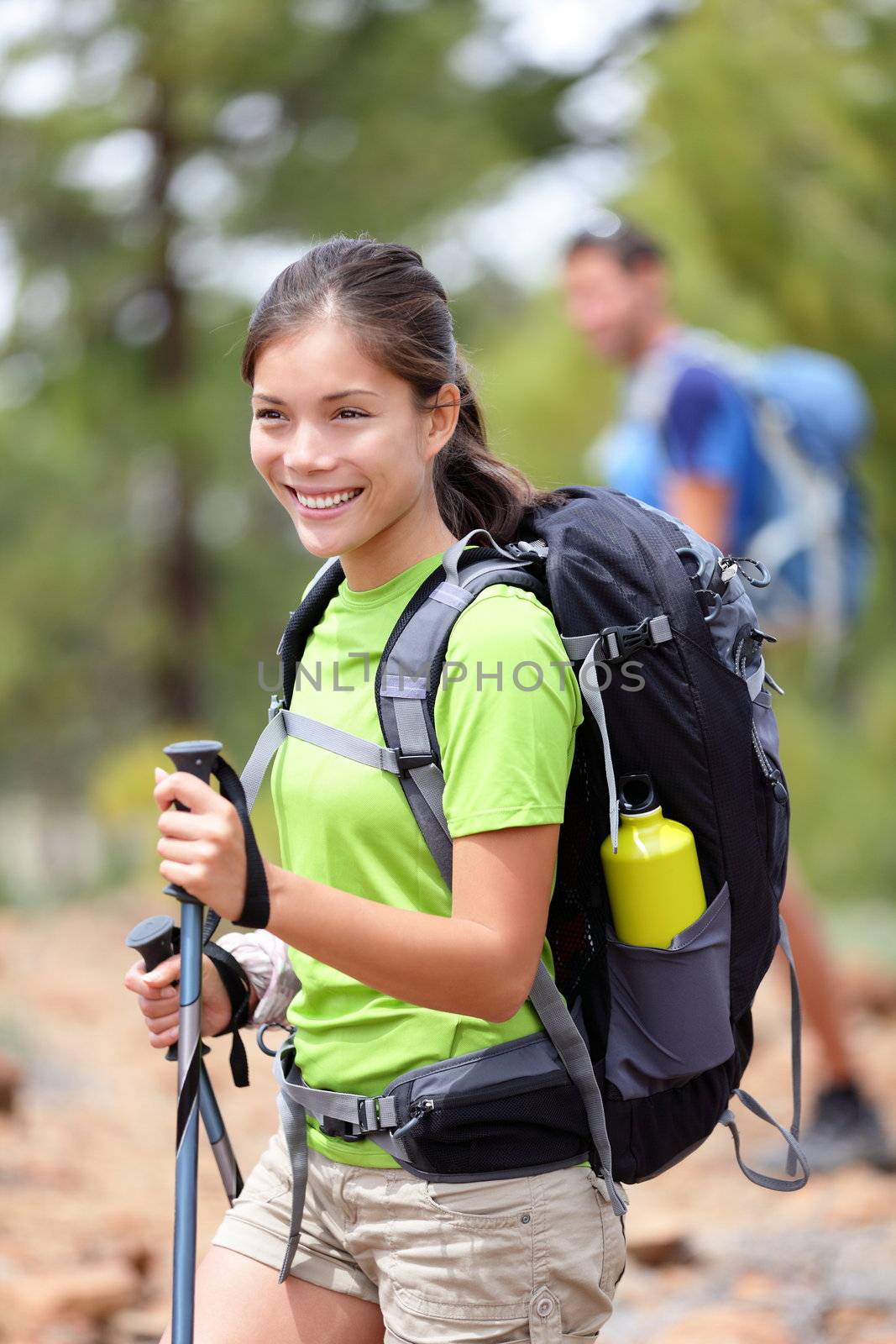 Hiking woman happy outdoors on hike in forest. Hiker in the background. Sporty active Asian Caucasian mixed race young woman smiling holding hiking sticks. Tenerife, Canary Islands, Spain