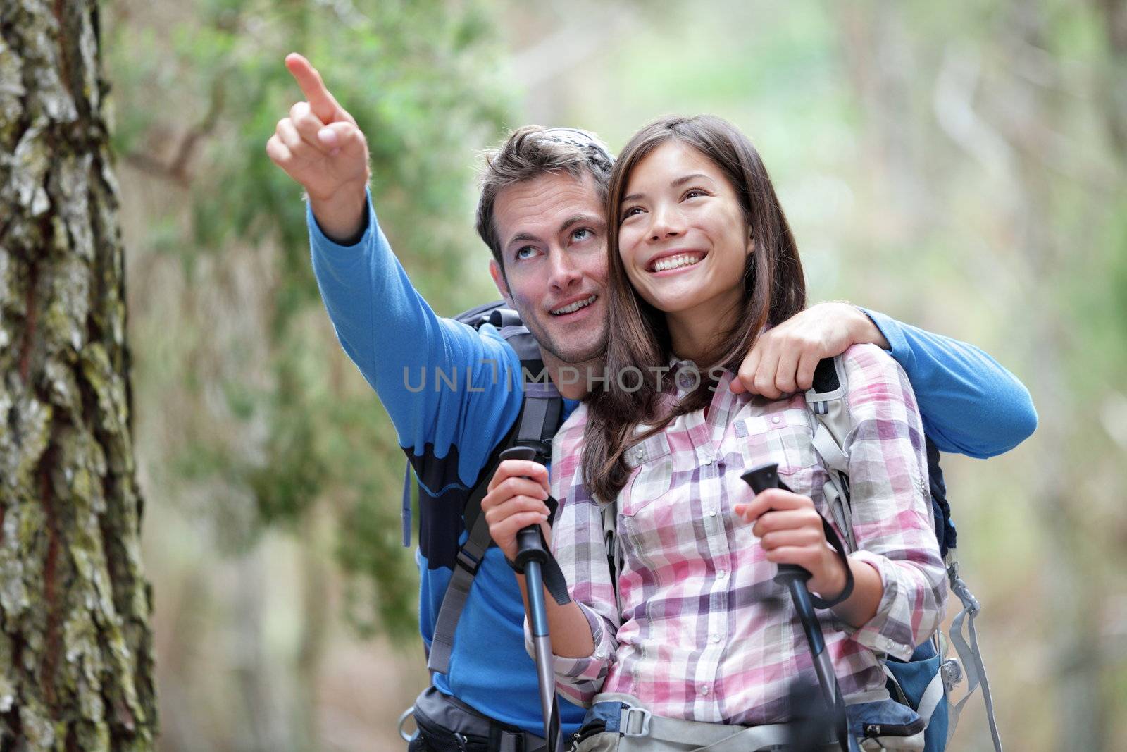 Happy couple hiking outdoors in forest. Active young asian woman hiker and caucasian man.