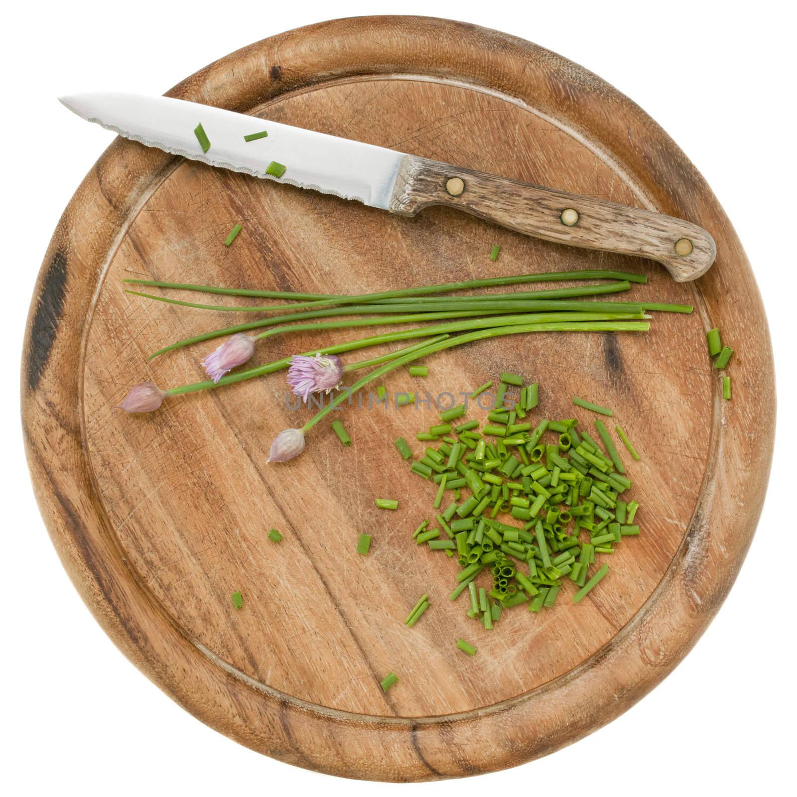 green chives with flowers chopped on a wood cutting board, isolated on white