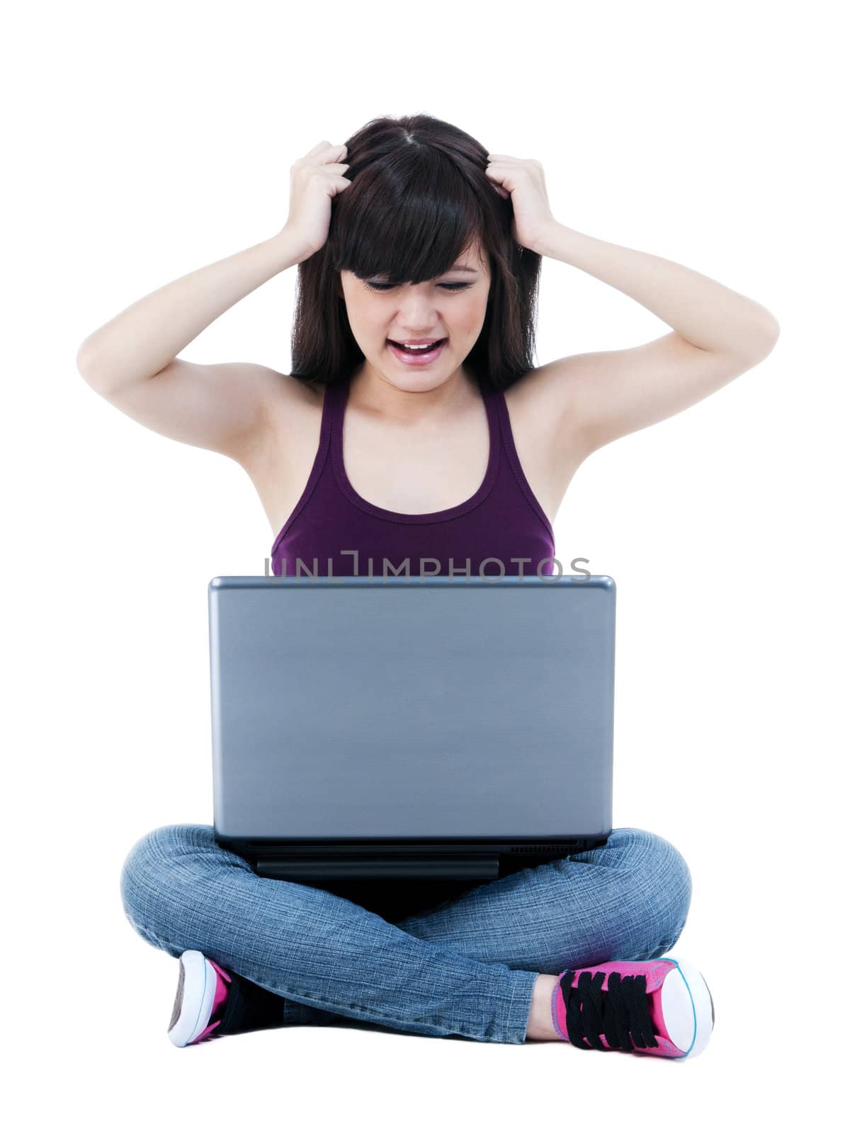 Frustrated young woman sitting on the floor with laptop and pulling her hair over white background.