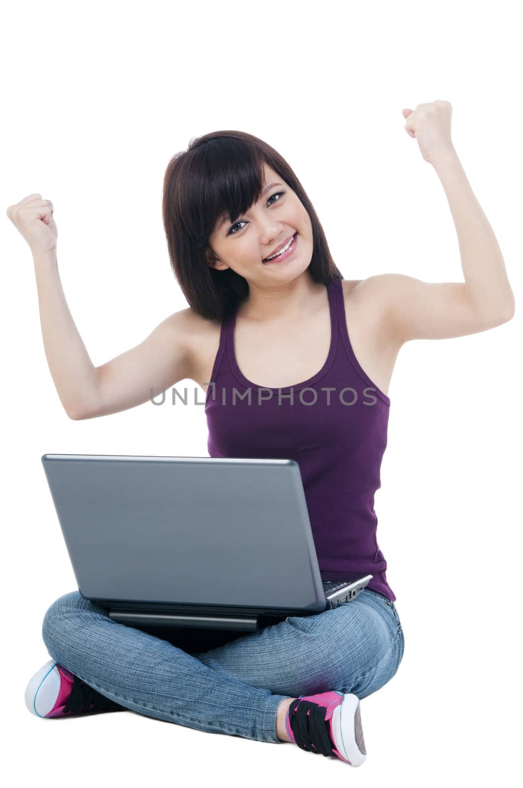 Portrait of a cute young woman sitting on floor with laptop and arms raised over white background.