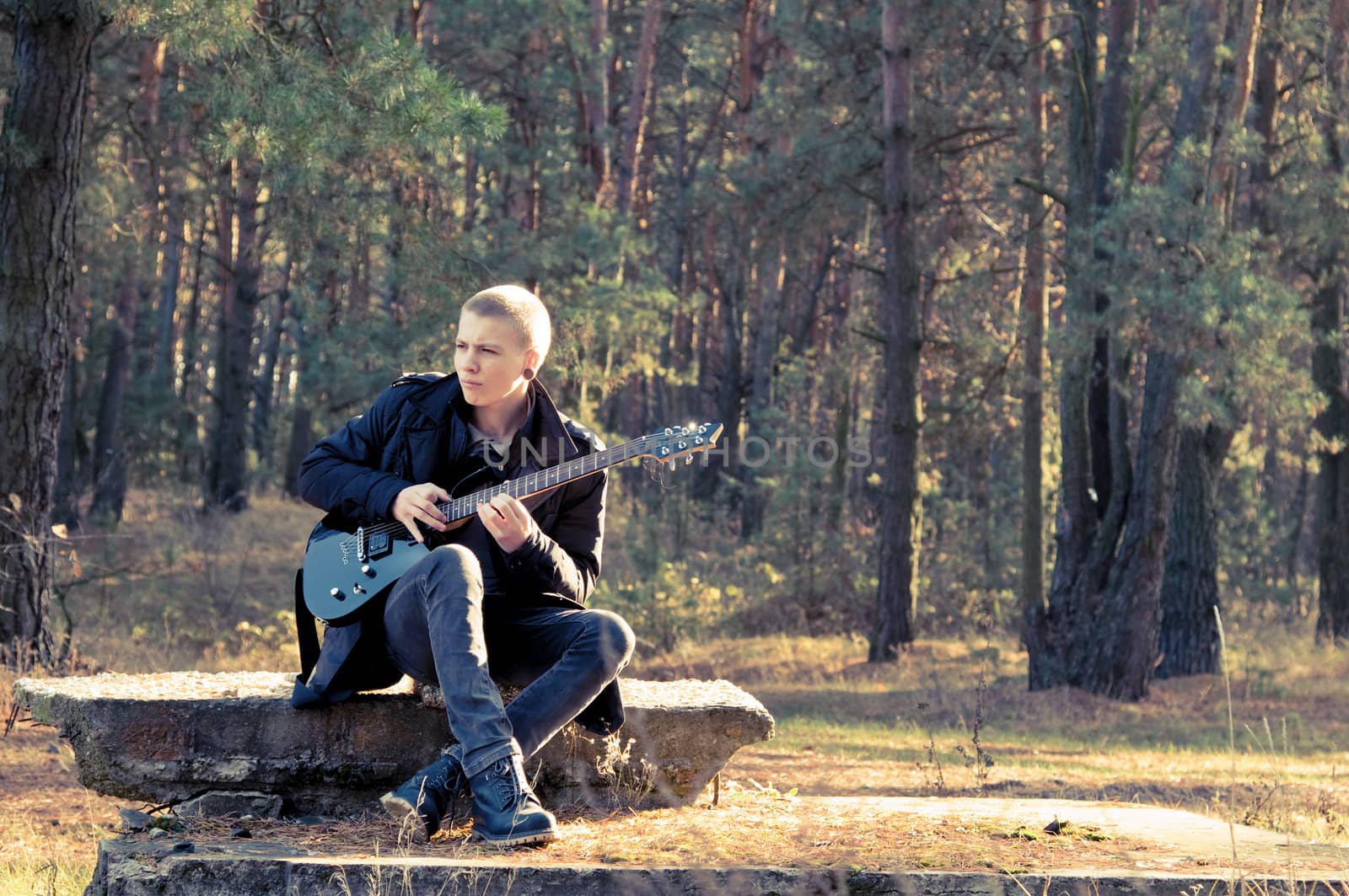 teen musician plays the guitar in the autumn forest