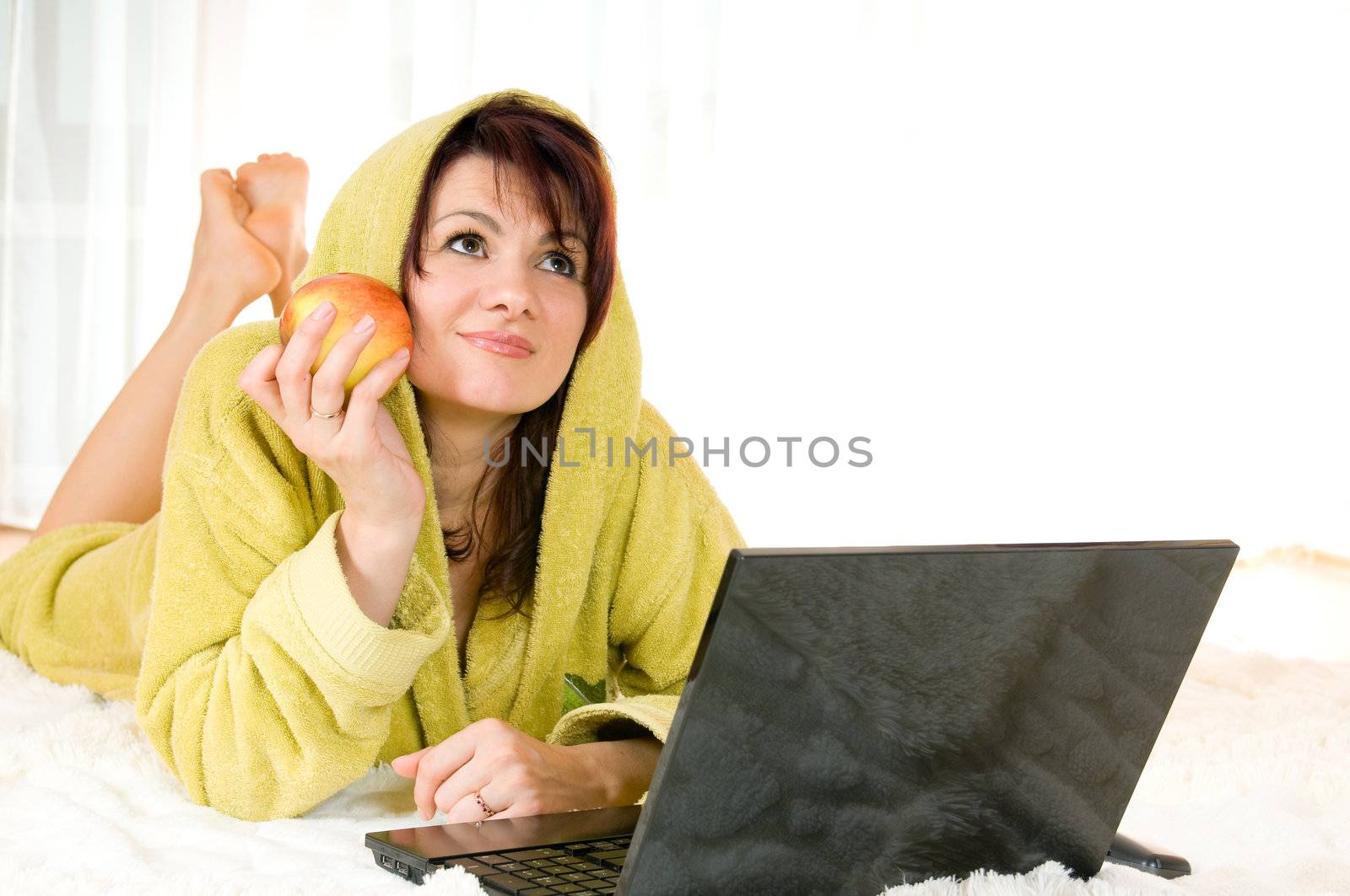 Woman in robe with laptop and apple lying on the floor