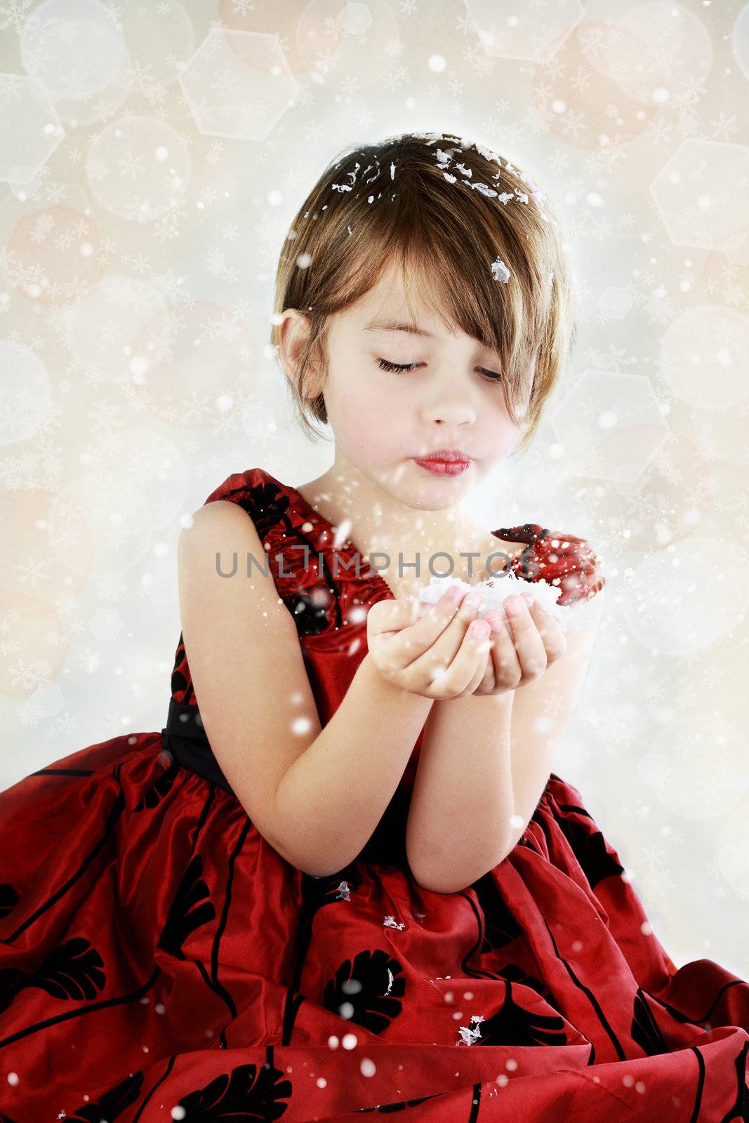 Little girl dressed up for the holidays blows snow from her hands.