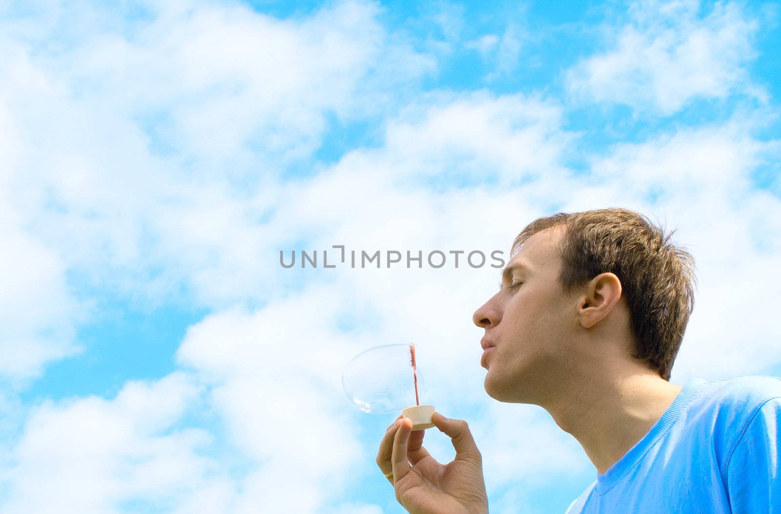 The young man starts up soap bubbles against the blue sky