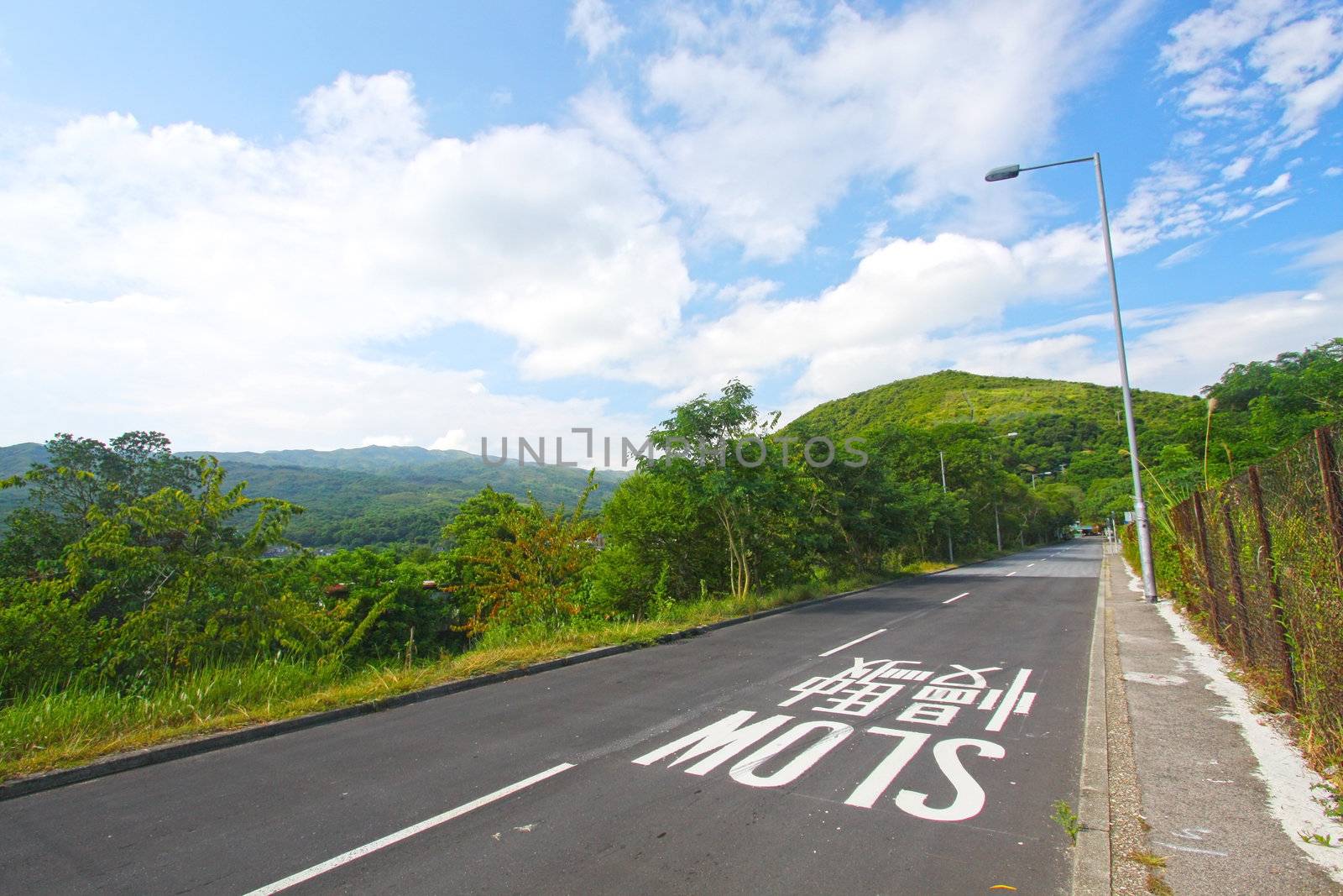 Road in a meadow against the blue sky with white clouds 