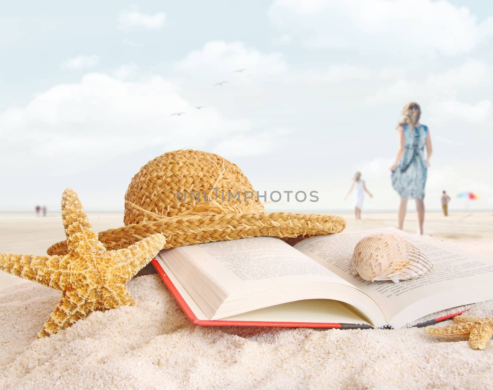 Straw hat , book and seashells on the beach with people walking