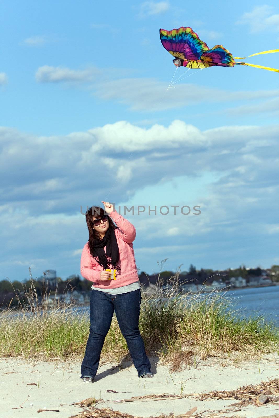 A young woman flying a kite at the sea shore on a nice day.