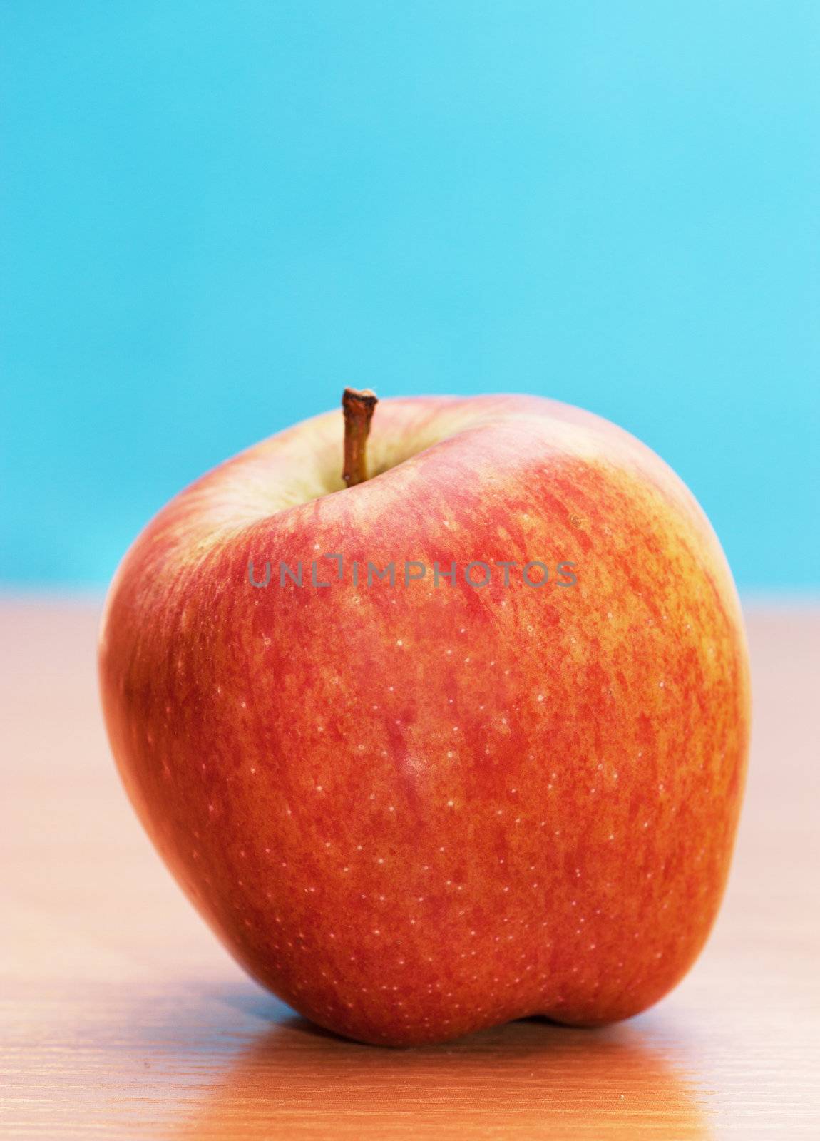 Big red apple on a table over blue background