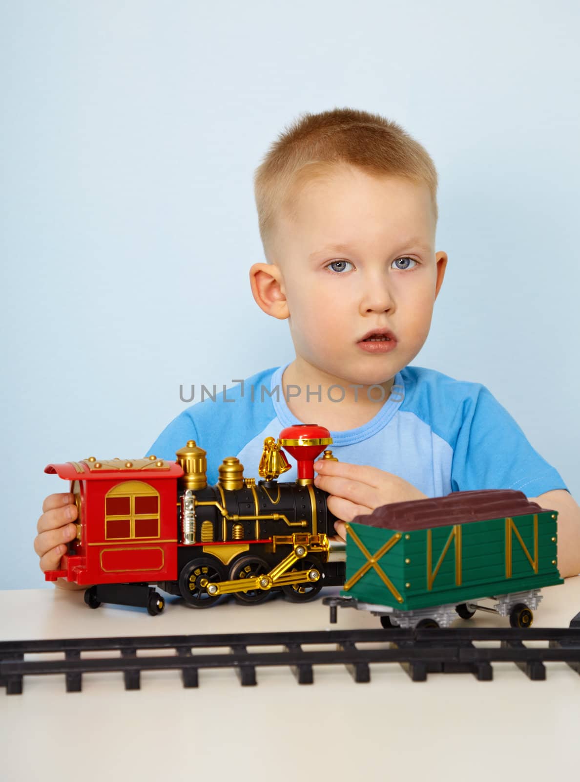 Little boy playing with a plastic toy locomotive on blue