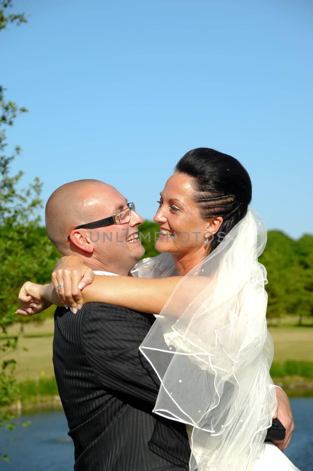 Groom is lifting his bride up in a park.