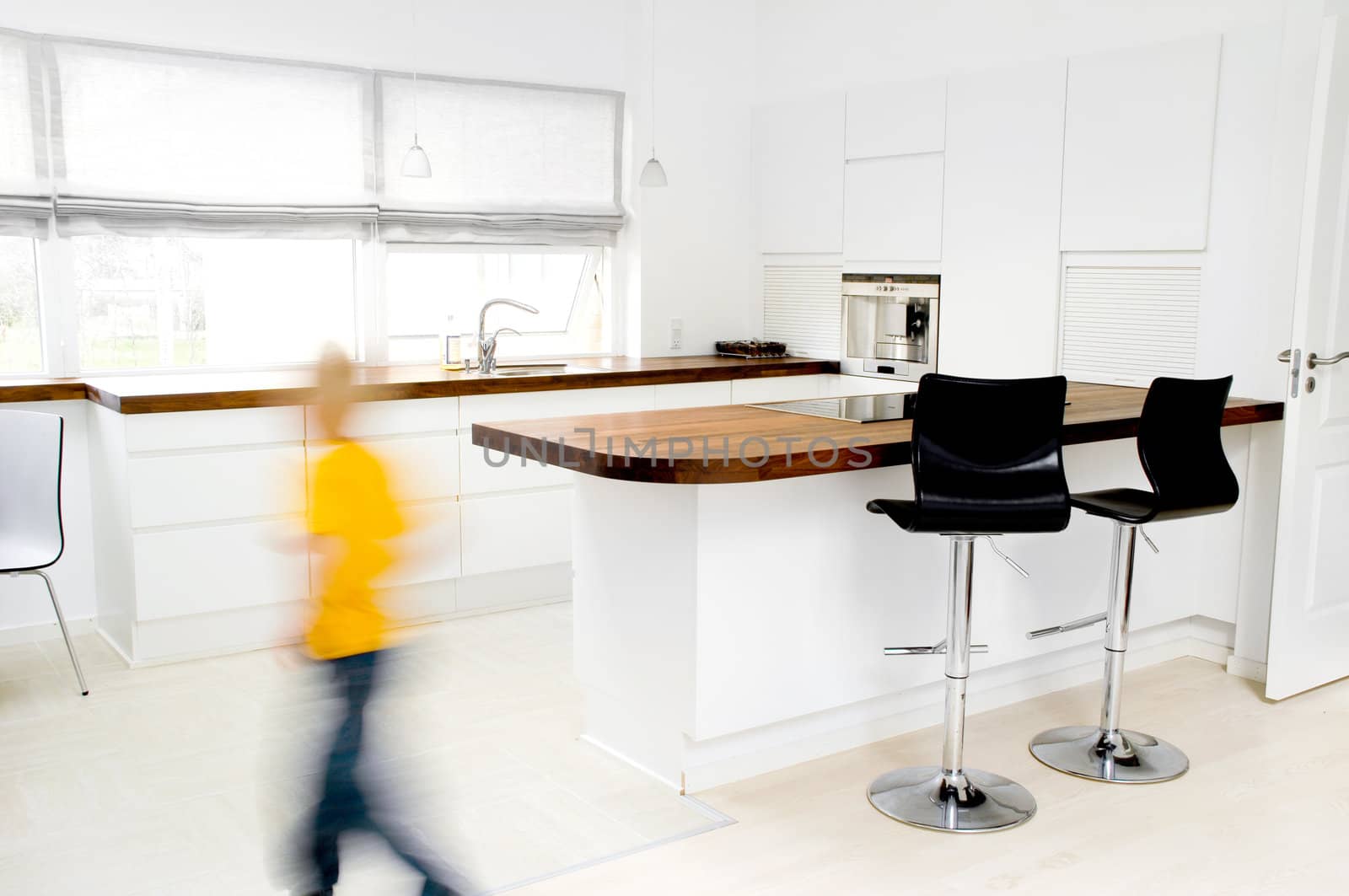 A modern white kitchen. Note the boy in the picture is in motion blur.