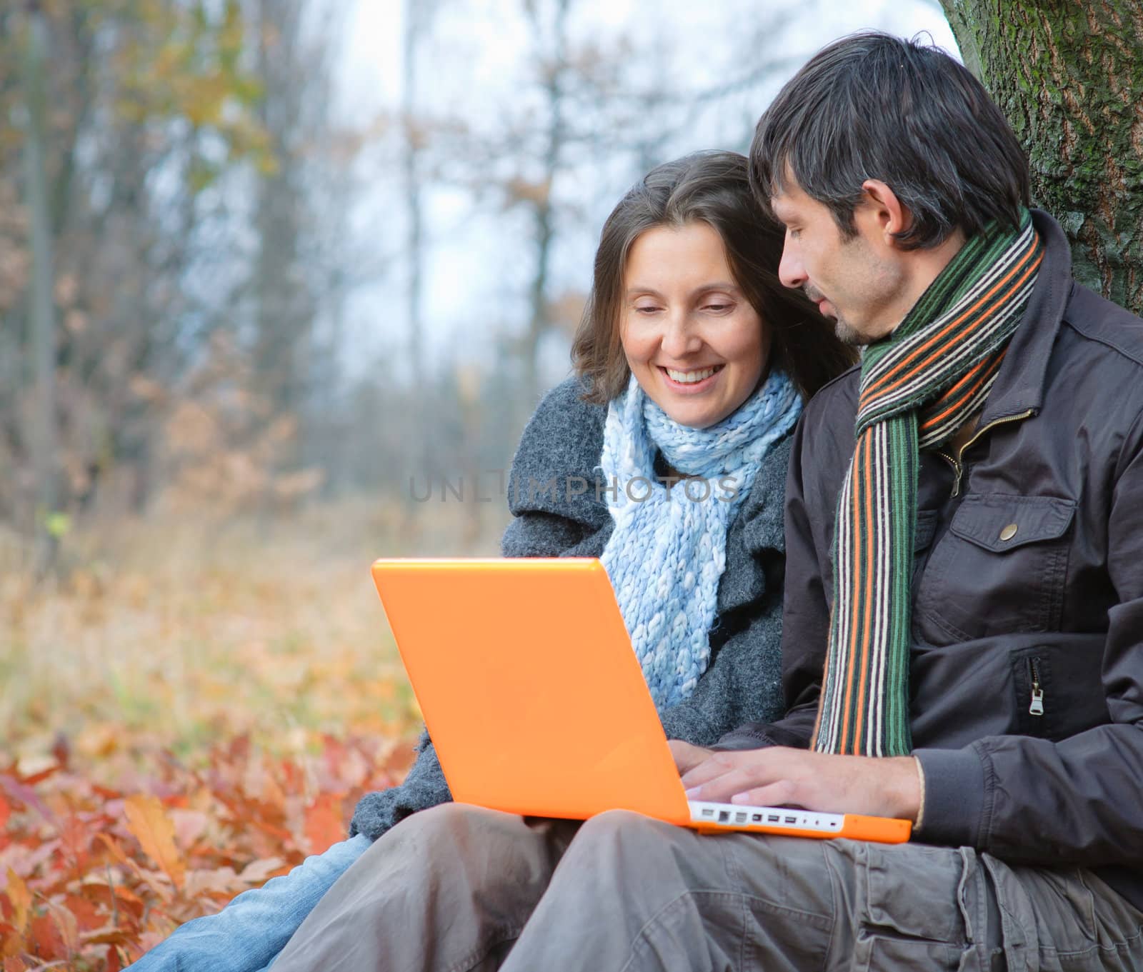 Romantic mature couple sitting with laptop in the autumn park.