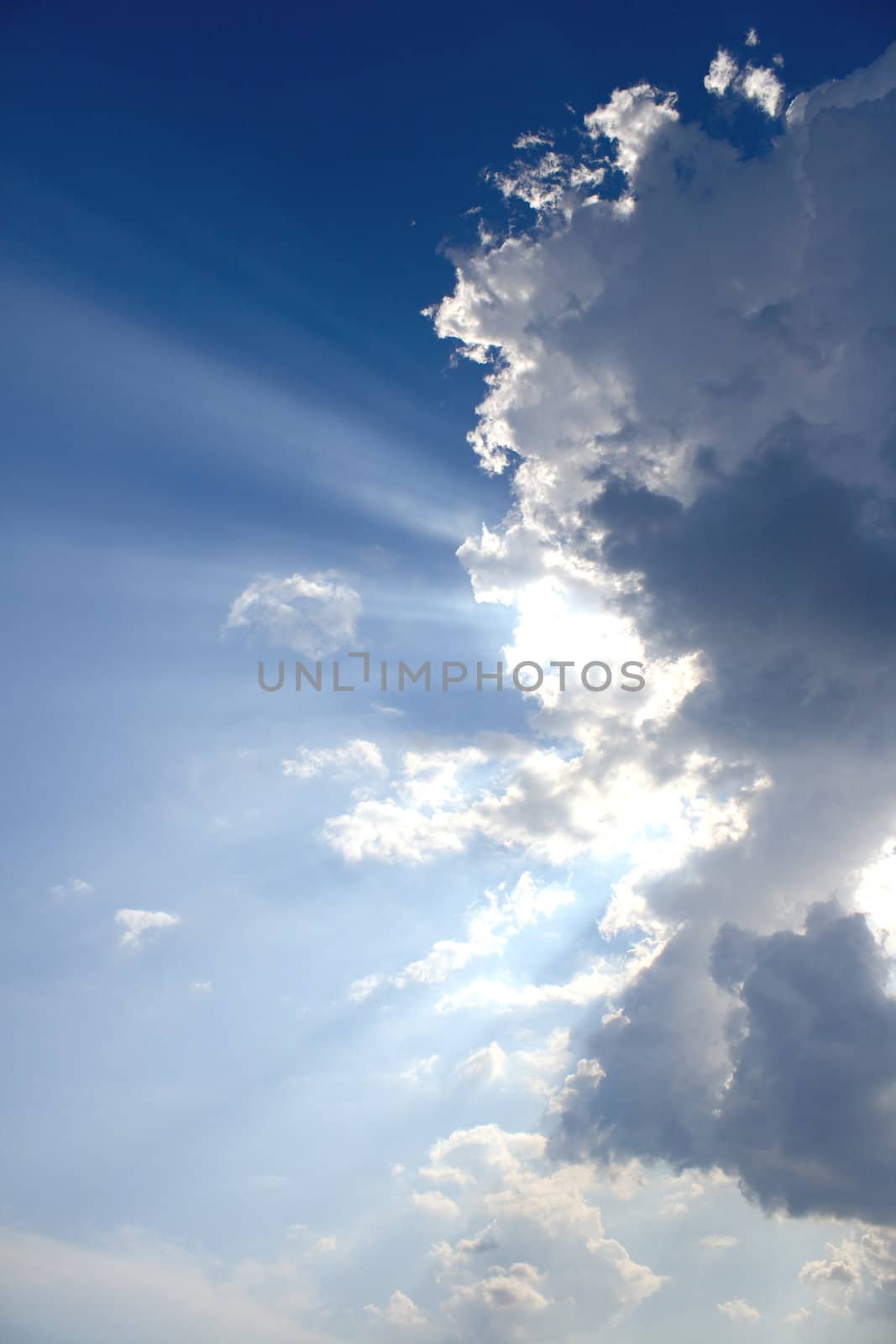 View of white and gray storm clouds in blue sky with rays of light