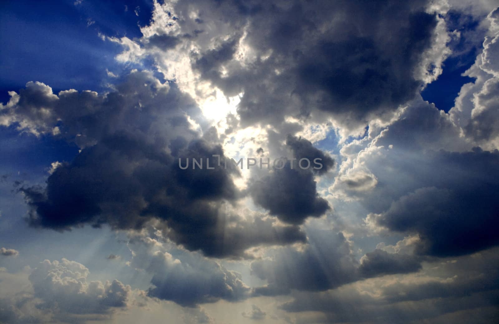 View of white and gray storm clouds in blue sky with rays of light